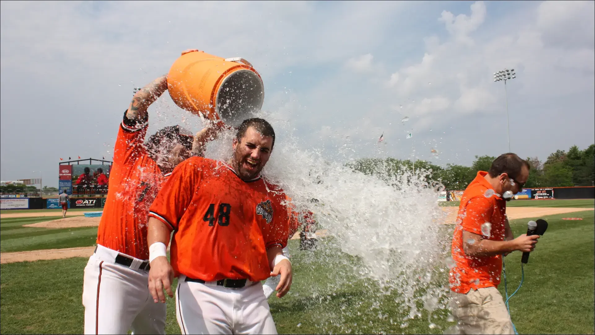 Baseball players in orange jerseys celebrate with a water-cooler splash.