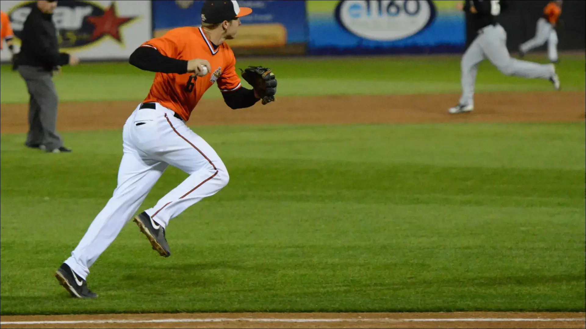 Baseball player in an orange jersey running on the field with the ball.