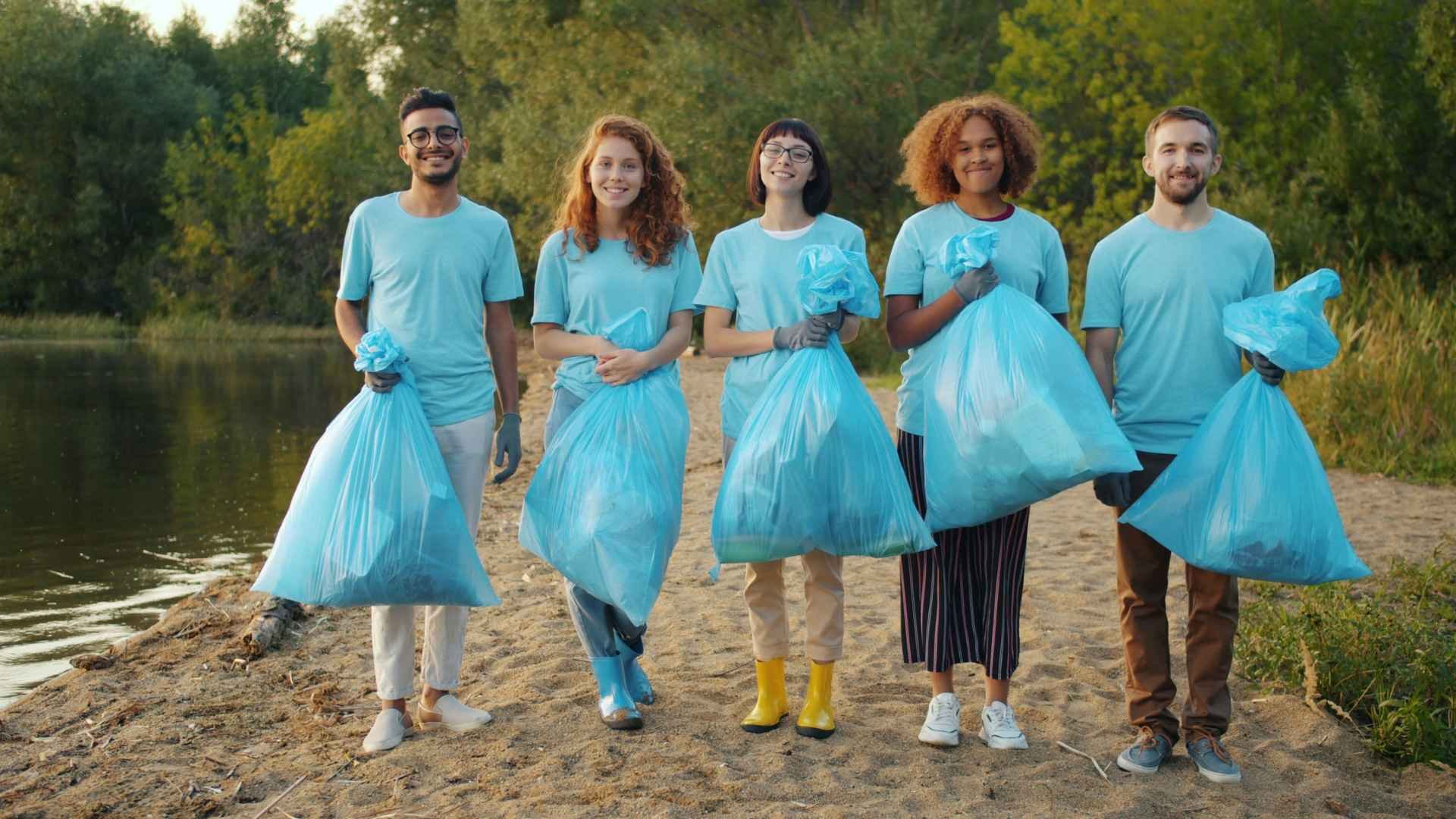 Group of smiling people standing by a river holding bin bags full of collected rubbish