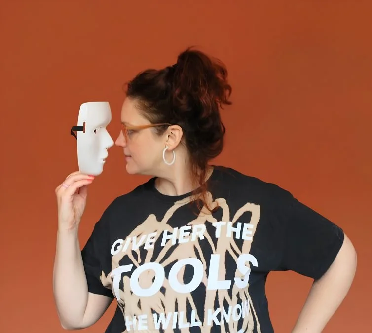  Susannah nose-to-nose with a white drama mask, wearing a t-shirt saying “give her the tools she will know what to do with them” 