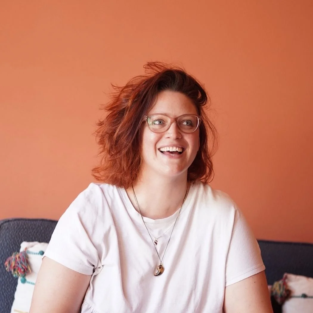  Susannah sitting on the sofa laughing, henna hair against a peachy-terracotta wall 