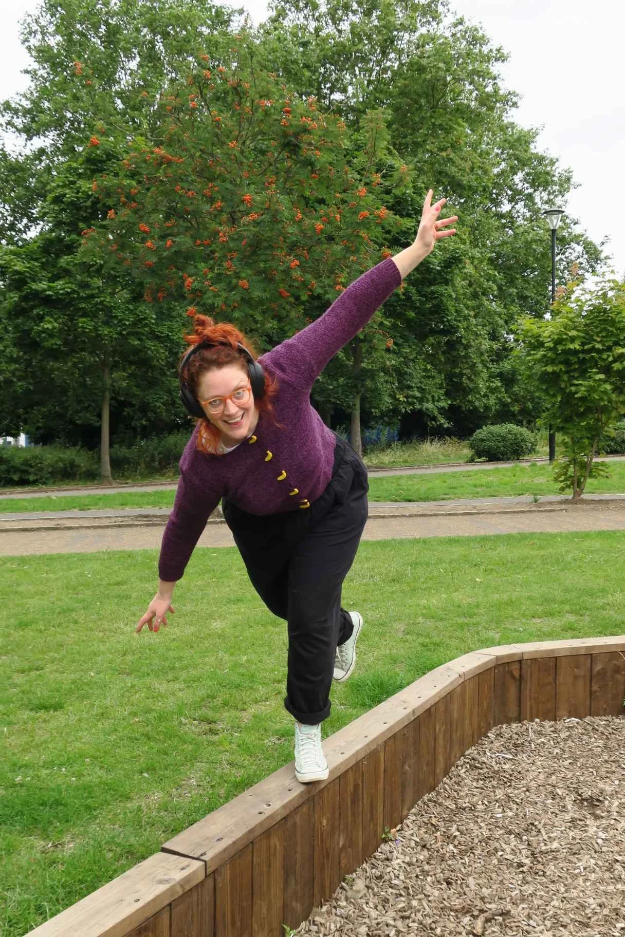  Susannah balancing on one leg on a narrow wall in the park, arms outstretched, smiling 