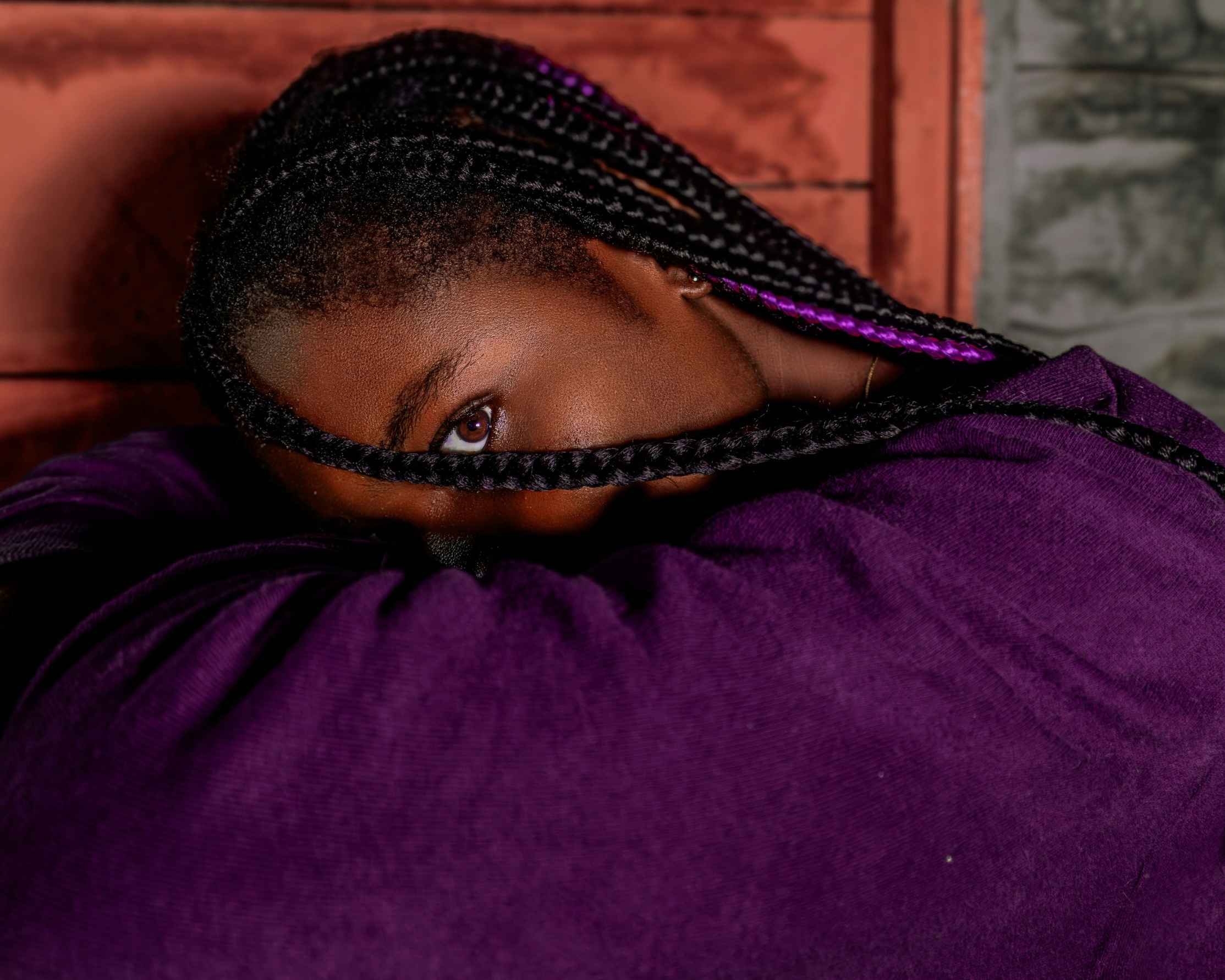 Girl with braids buries her face in her arms, one eye peeping out