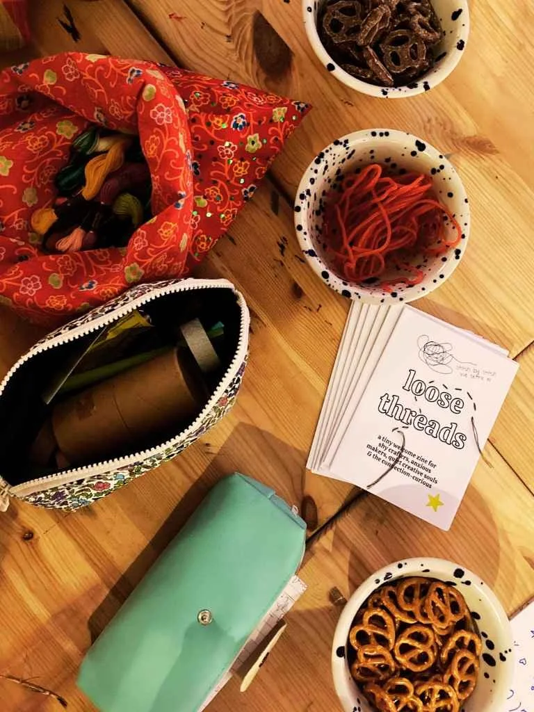 Cluttered tablescape from above with Loose Threads handmade zines, party snacks and craft materials