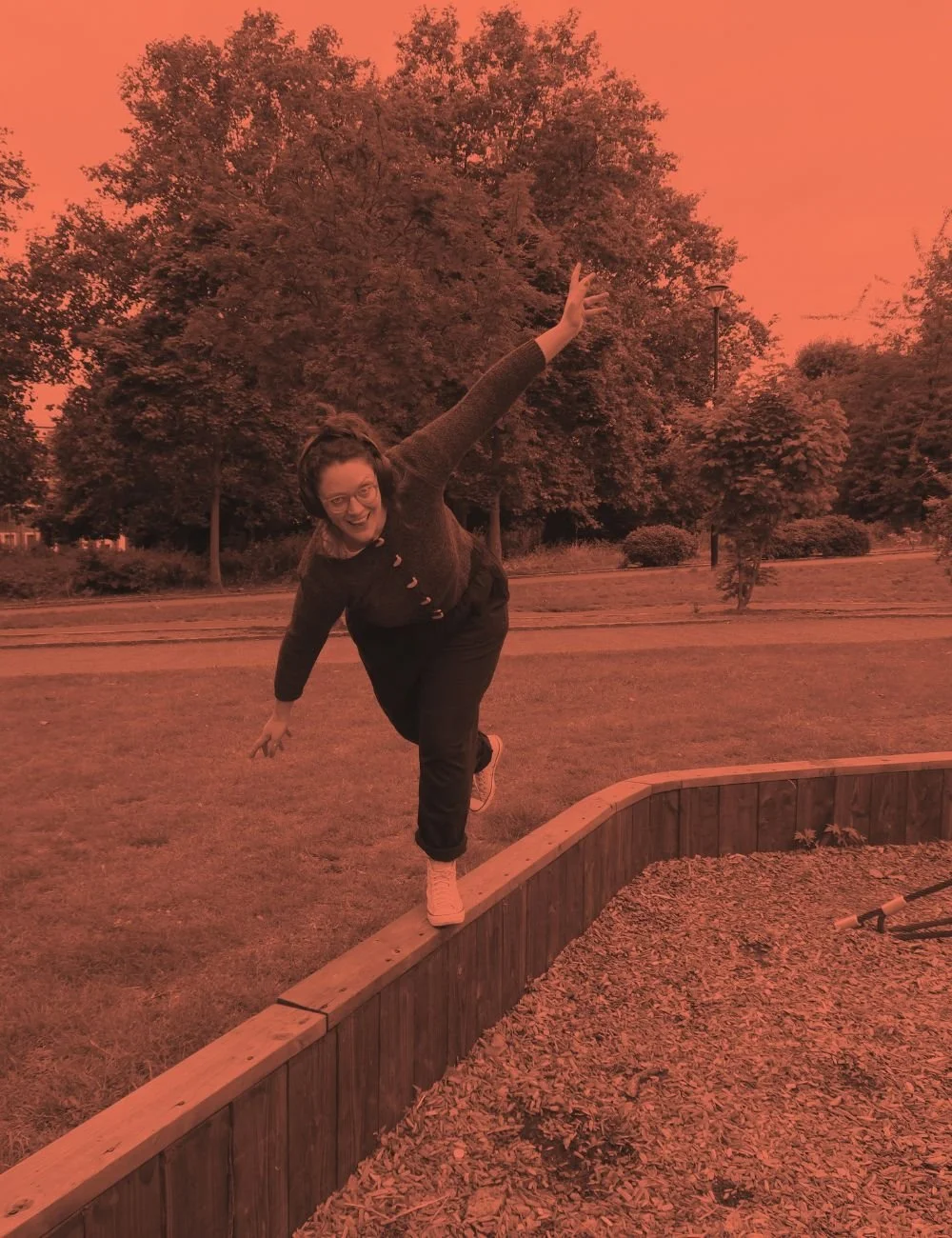 Susannah balancing on one leg on a narrow wall, arms outstretched, a bit wobbly, picture tinted Gutsy-brand peachy terracotta colour