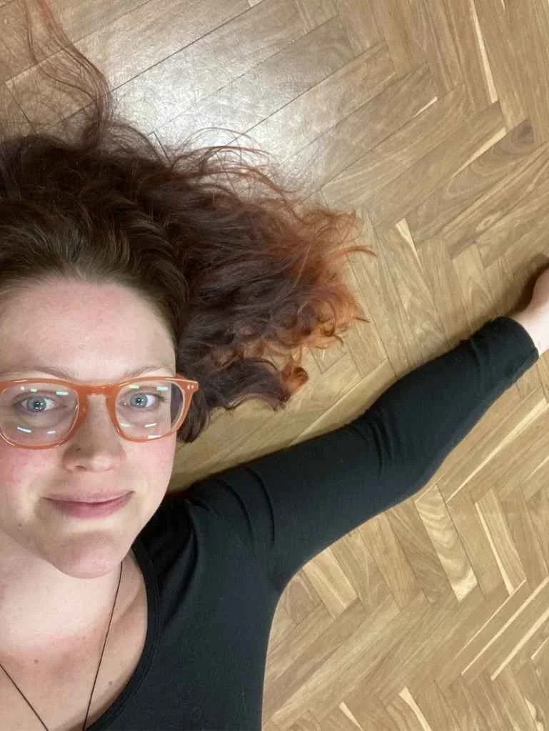 Susannah lying on the floor after a workshop, arm outstretched, smiling