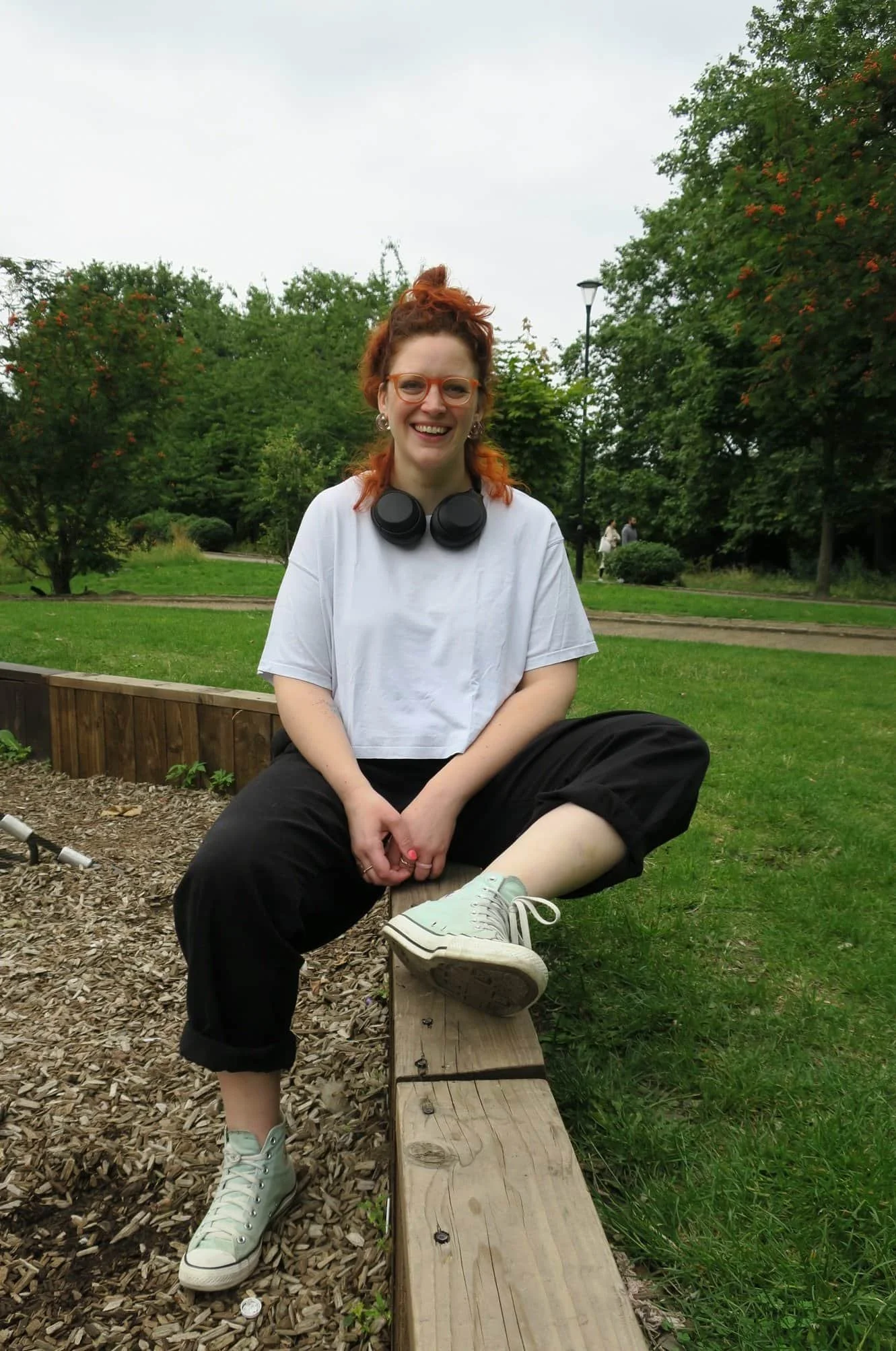 Gutsy founder Susannah sits on a wall in the park, smiling, headphones round her neck