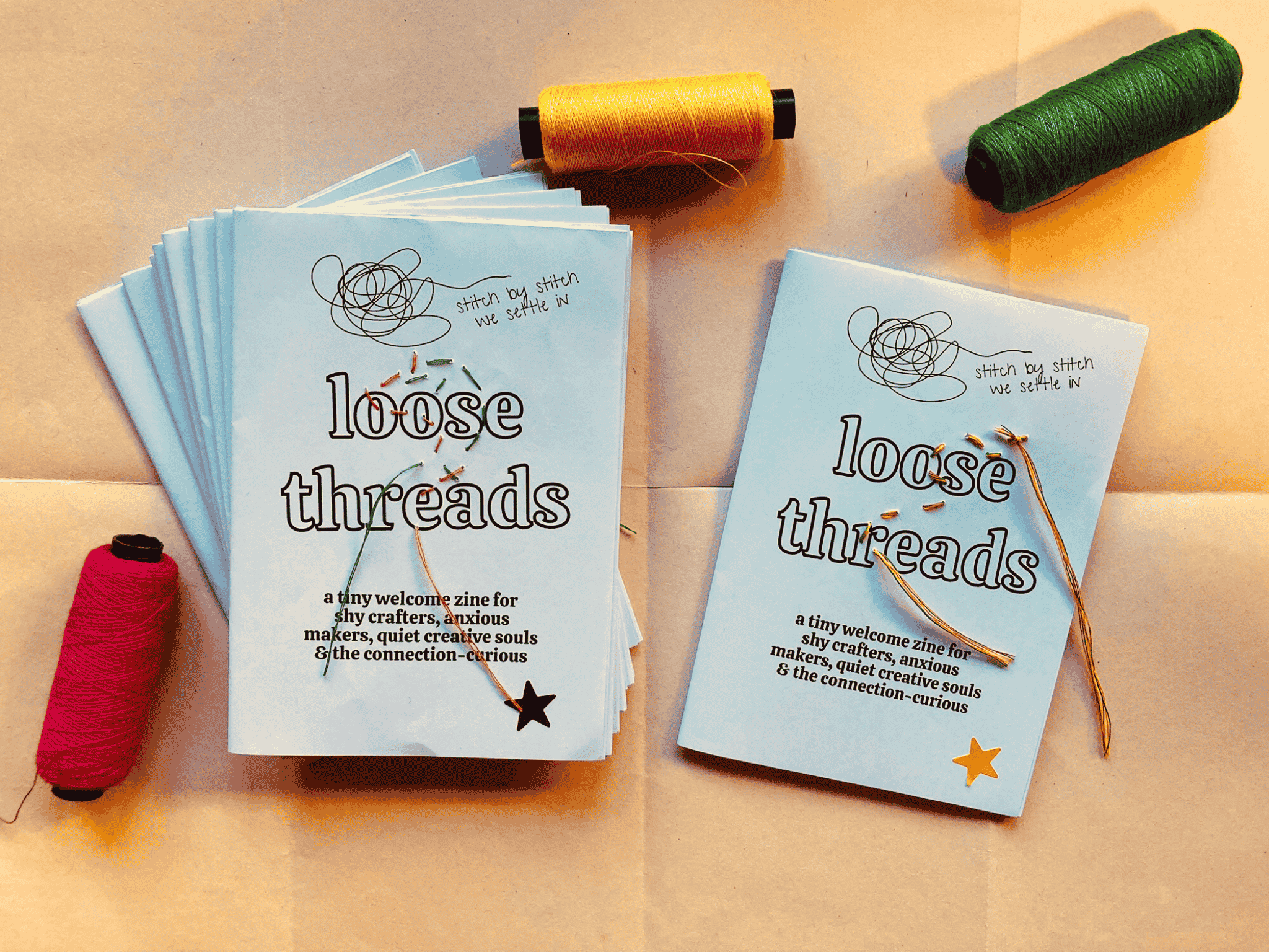Handmade Loose Threads welcome zine photographed with colourful spools of thread, created to support shy and anxious participants with gentle prompts and reassurance during and after the gathering.