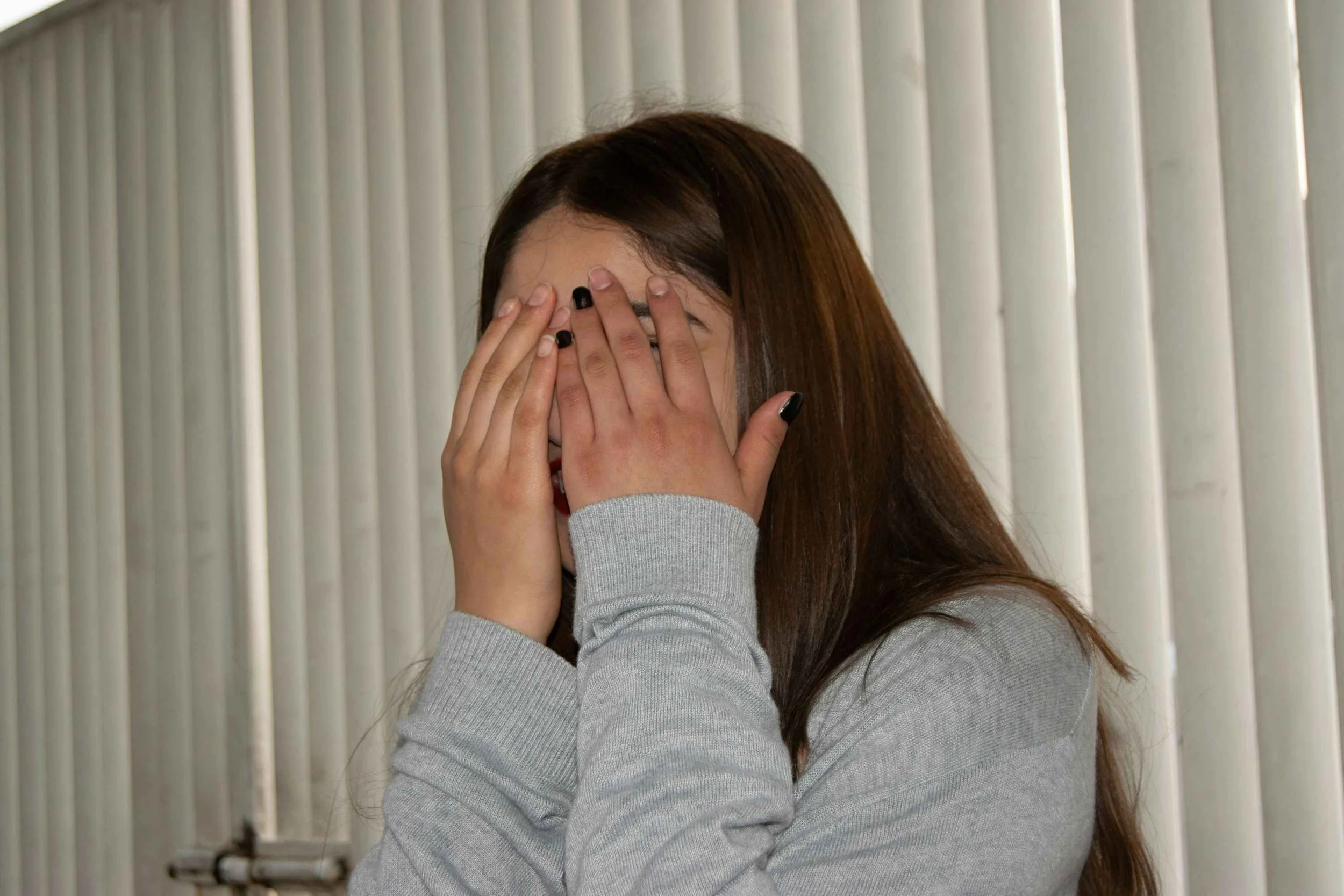 Girl with dark-blonde hair hides her face with both hands