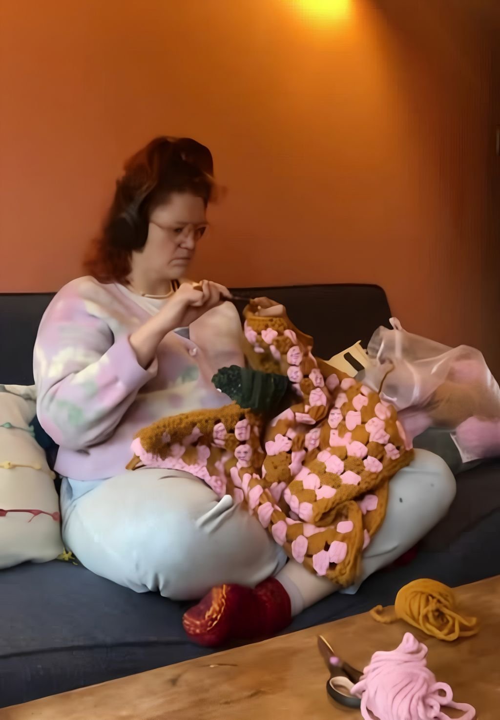 Susannah sitting on a sofa making a crochet jumper in Gutsy brand colours!