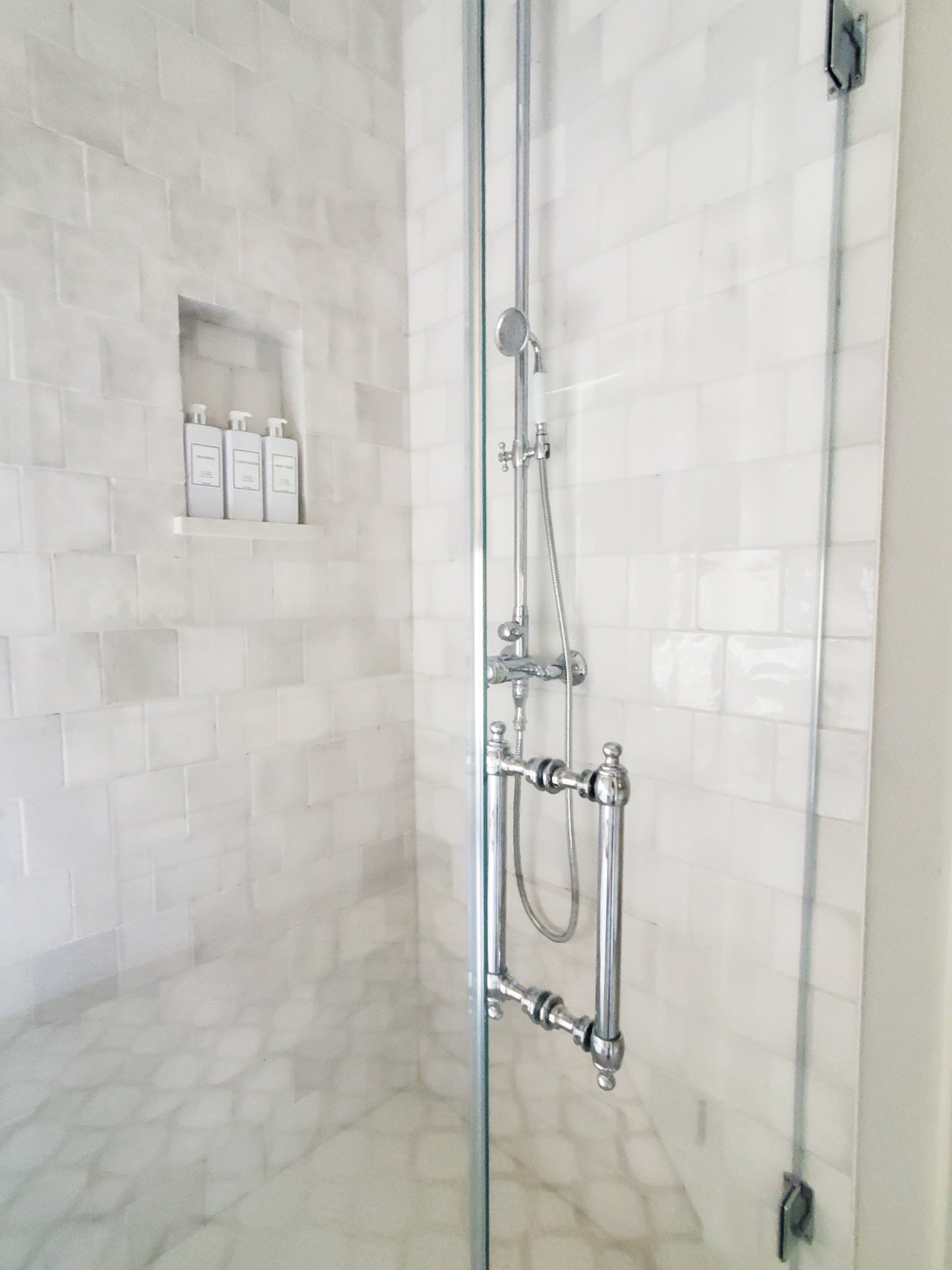 A glass shower enclosure with white square zellige tile on the wall and polished chrome shower fixture in a primary bathroom in McKinney, Texas. Interior Design by Samantha Leonard Designs