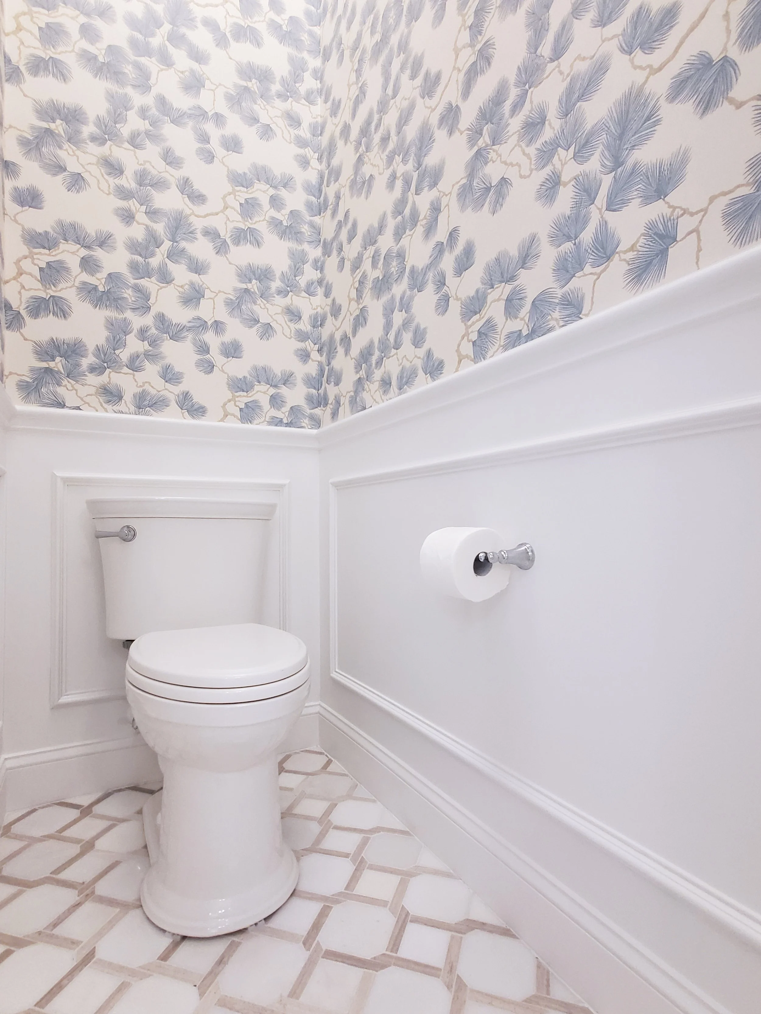 White toilet with white wainscotting with blue floral wallpaper above in a Primary Bathroom in McKinney, Texas. Interior Design by Samantha Leonard Designs