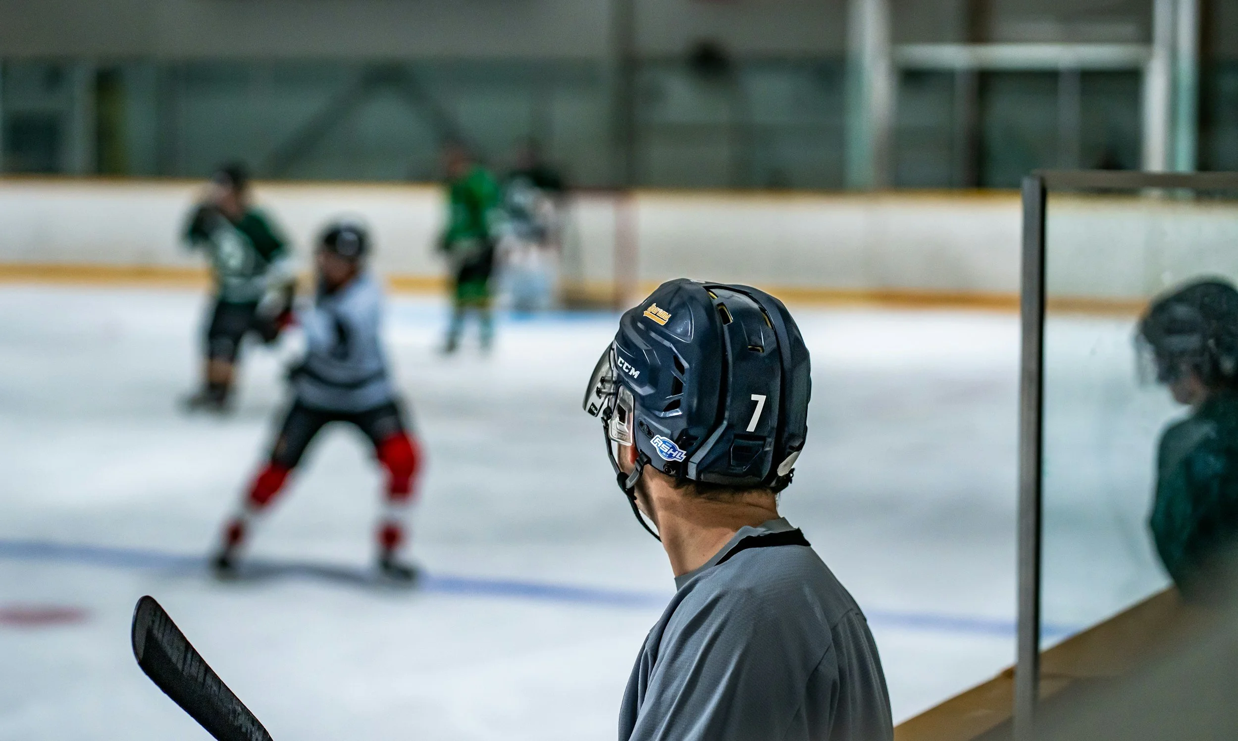 Hockey player with helmet standing on the bench in rink, watching the game.