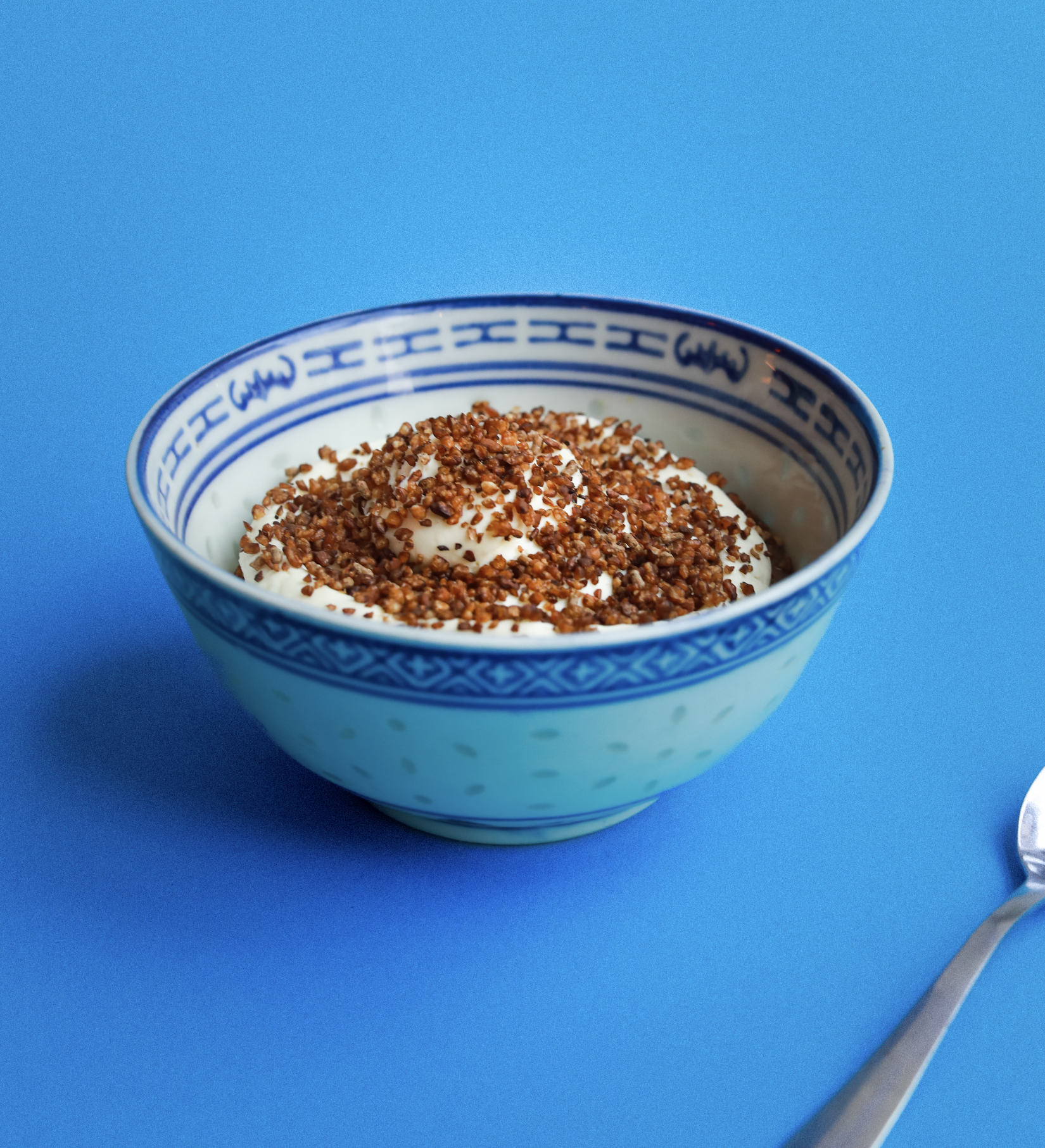 Bol de yaourt nature garni de noix hachées sur fond bleu.