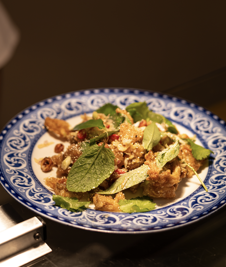 Salade de viande avec des feuilles de menthe et diverses herbes sur une assiette décorée en bleu et blanc.