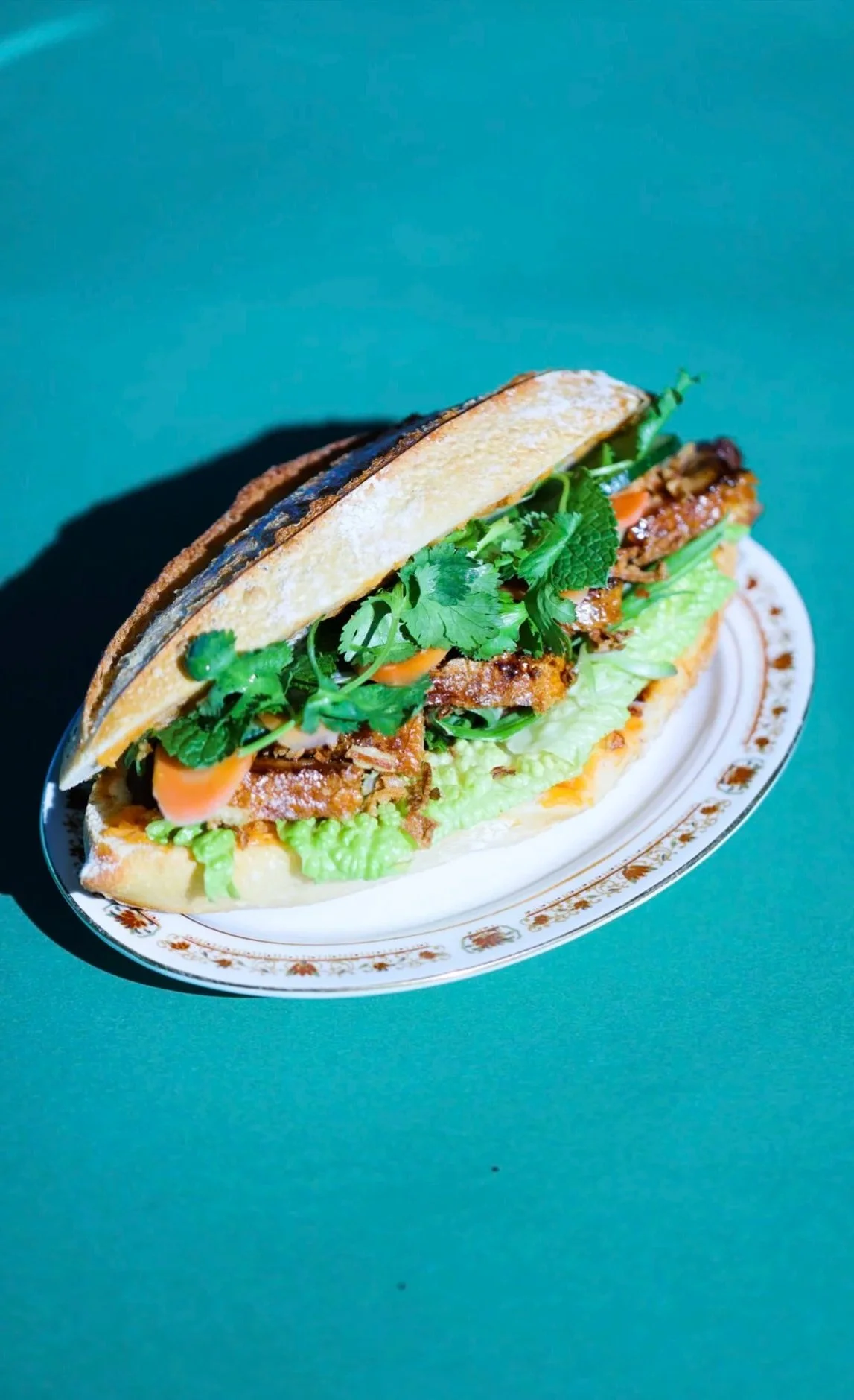 Bánh mì vietnamien avec viande, légumes frais, coriandre, dans un bol décoratif, sur fond vert.