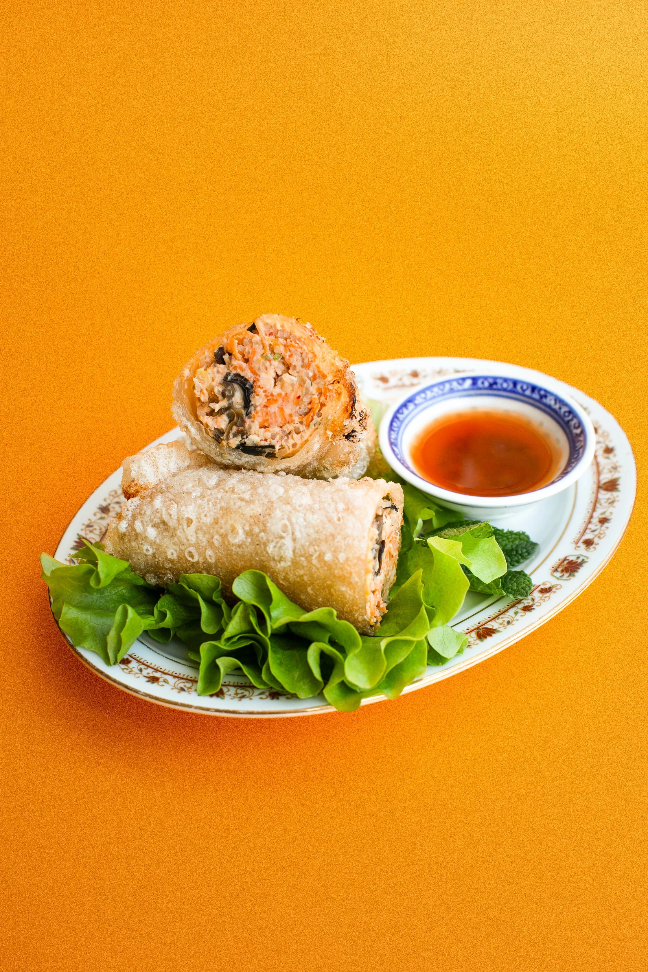 Rouleaux de printemps avec sauce, garnis de laitue et de brocolis, servis sur une assiette décorée.
