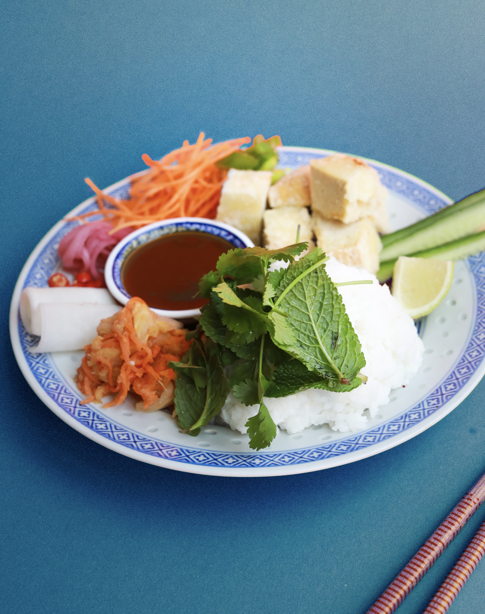Assiette de nourriture asiatique avec poulet, riz, légumes, sauce, citron, herbes, et accompagnements.