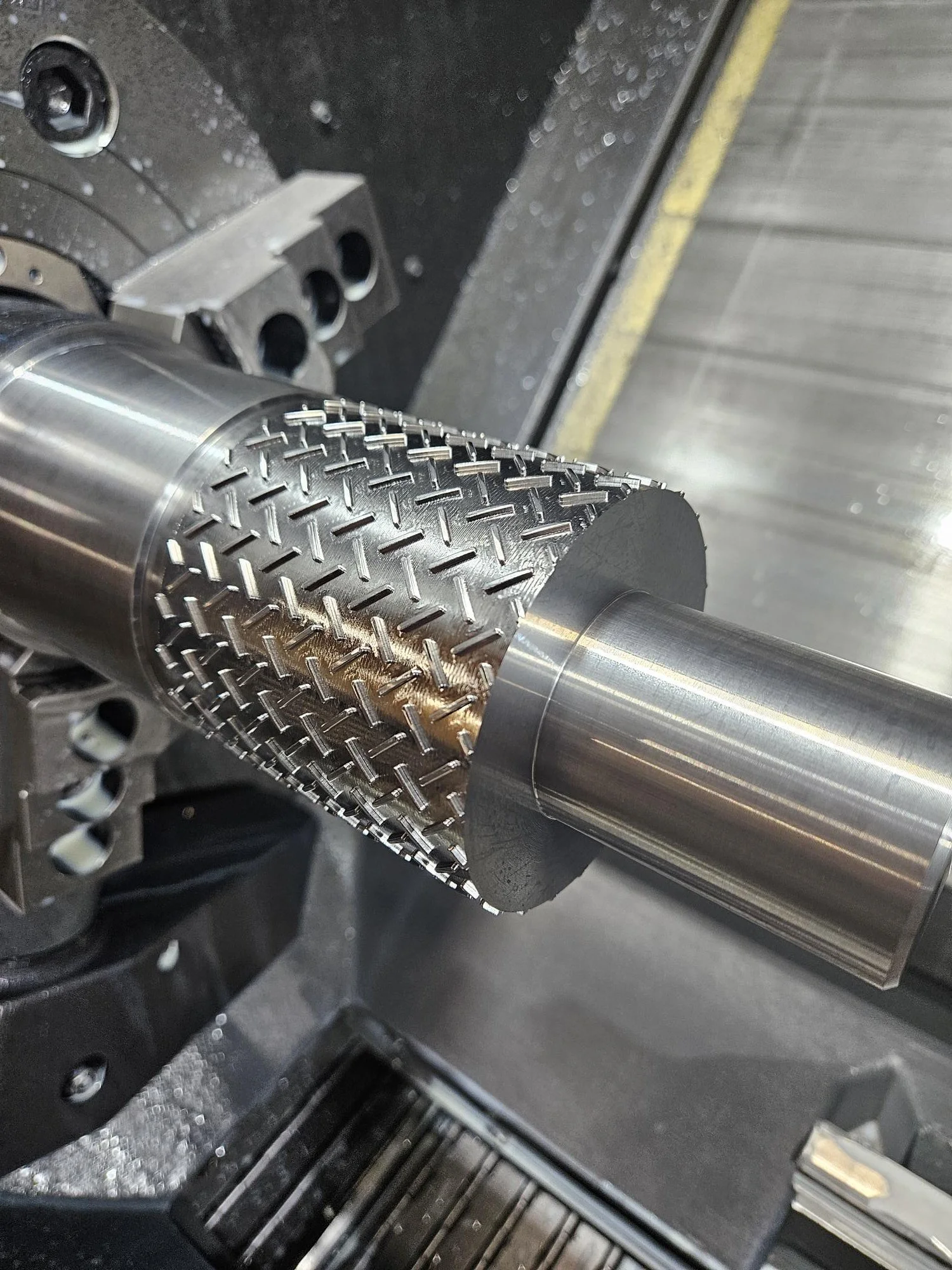 Close-up of a metal cylinder with diamond-patterned knurling inside a machine.