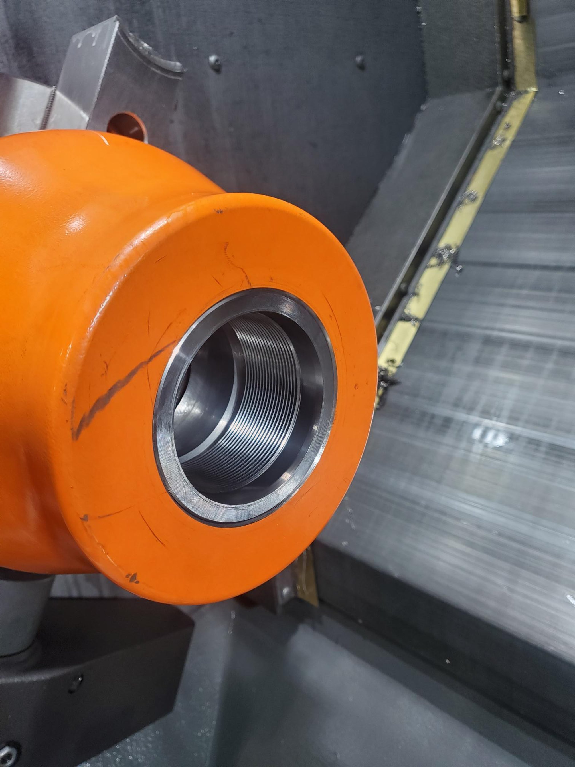 Close-up of an orange cylindrical industrial part with metal threading inside, possibly part of machinery or equipment.