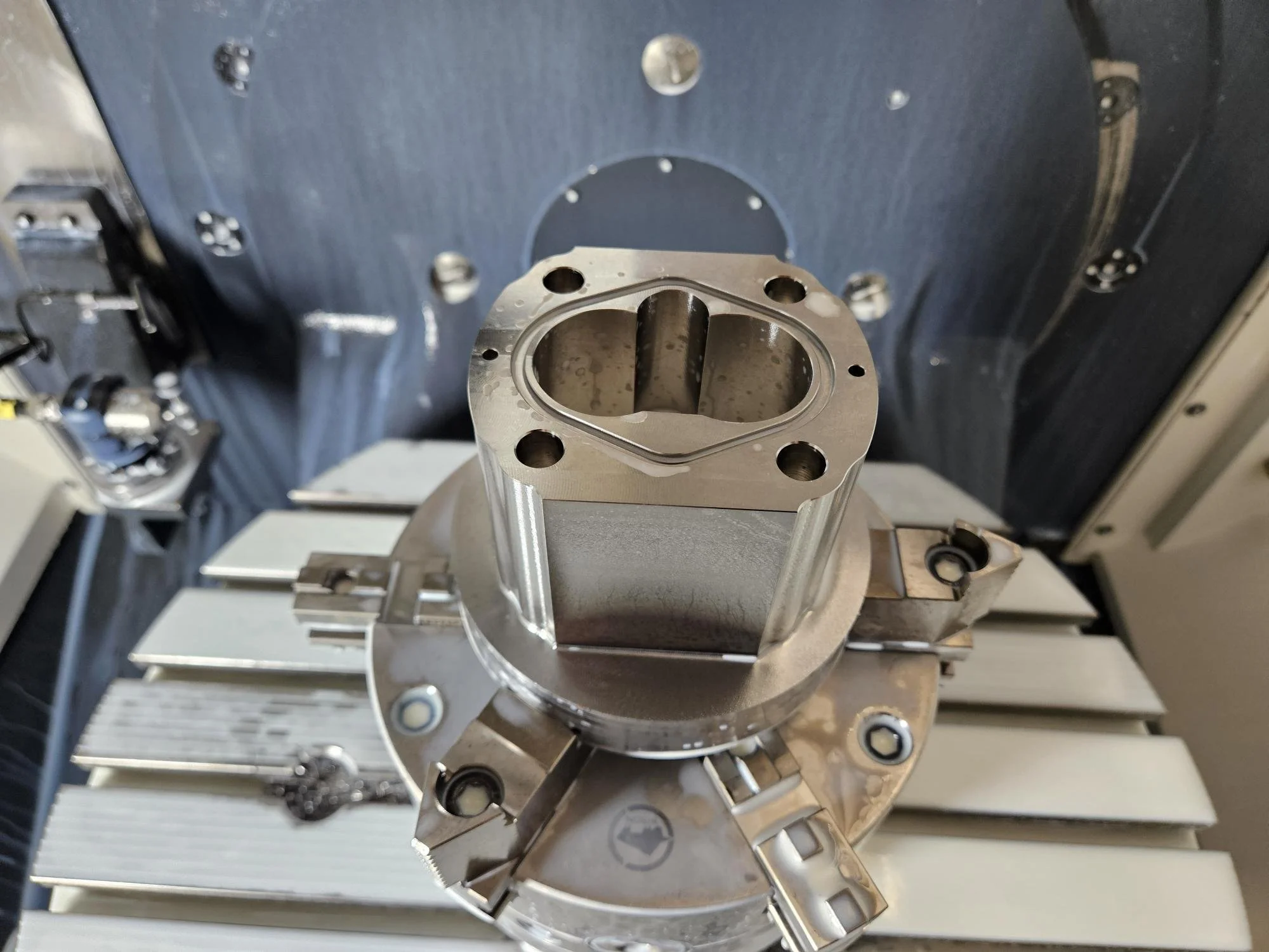 Metal cylinder part inside a CNC machine with tools and fixtures visible.