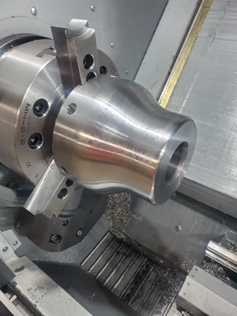 Metal part being machined on a lathe, with metal shavings around.