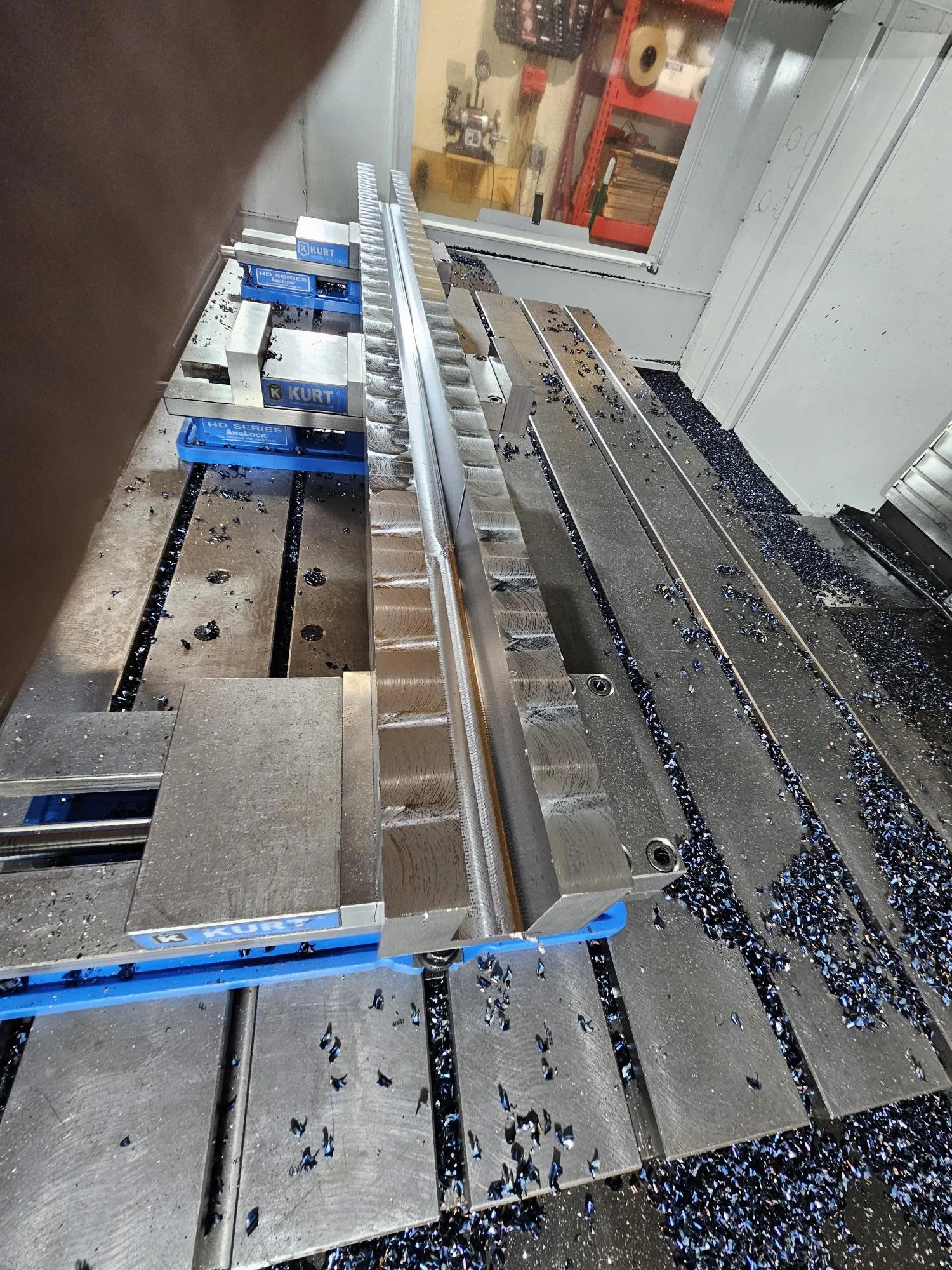 Metalworking machinery with metal shavings and a workpiece secured in a vice clamp, possibly in a CNC milling machine.