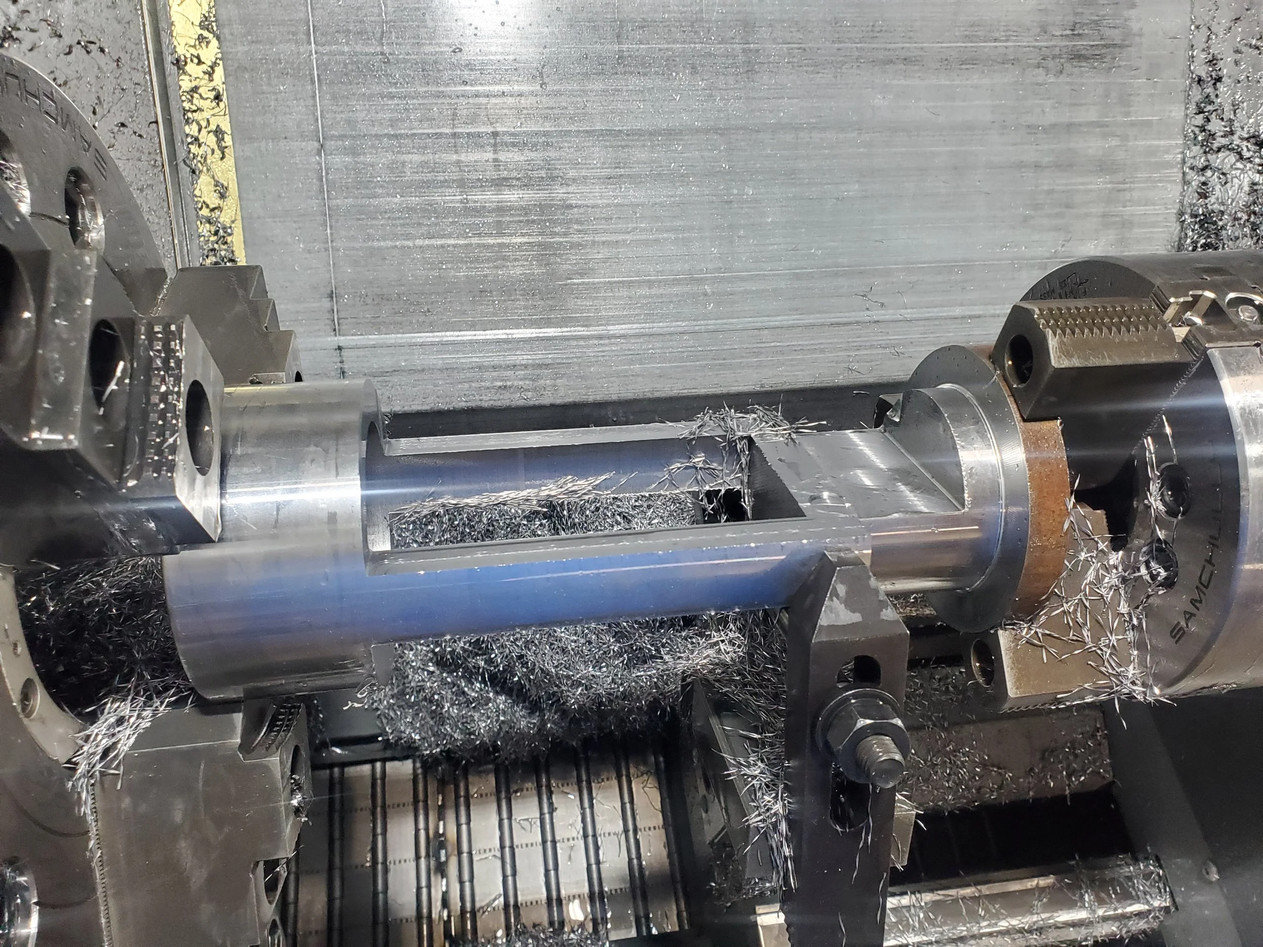 Metalworking lathe machine with metal piece being machined, surrounded by metal shavings.