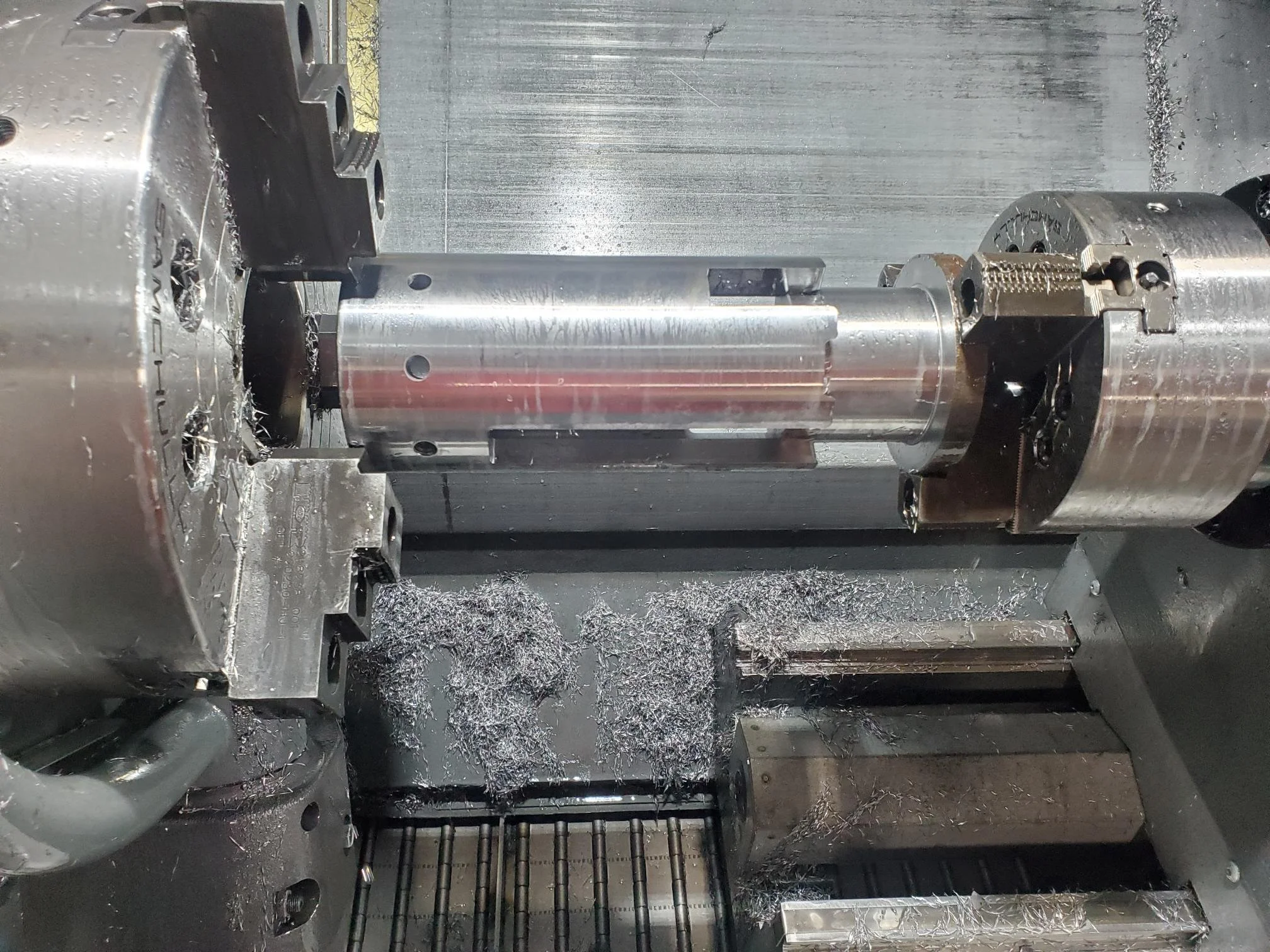 Metal lathe machining a cylindrical component, with metal shavings visible.