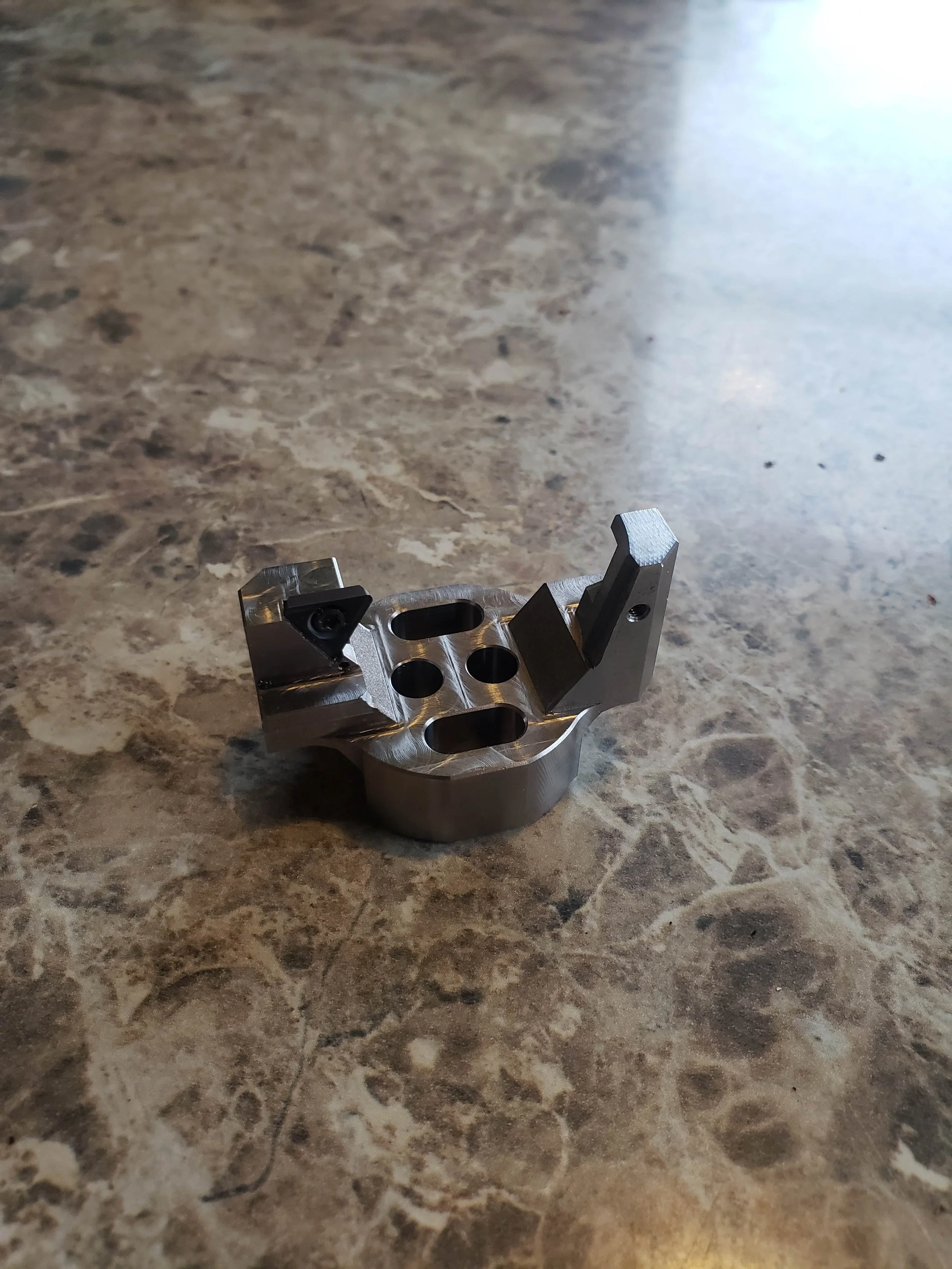 Metal component with holes and angular features on a marble surface.