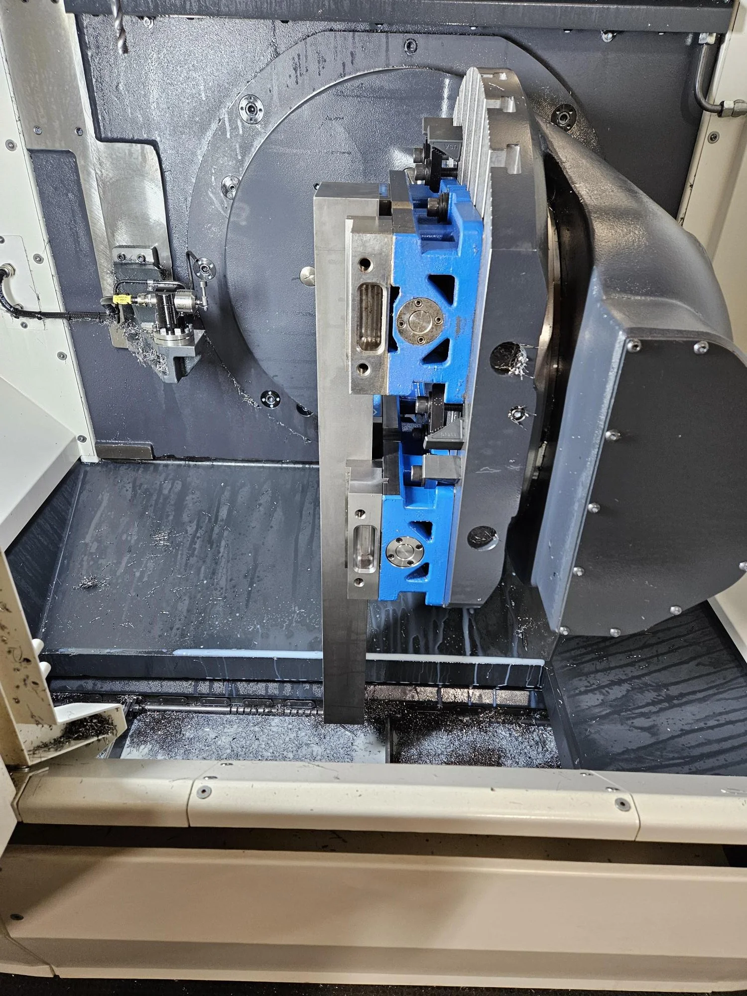 Close-up of a CNC machine with a metal piece being processed, featuring a blue vise and some metal shavings.