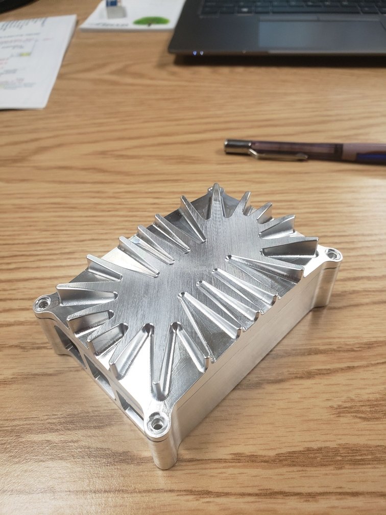 Aluminum heatsink on a wooden table with a pen and a laptop in the background.