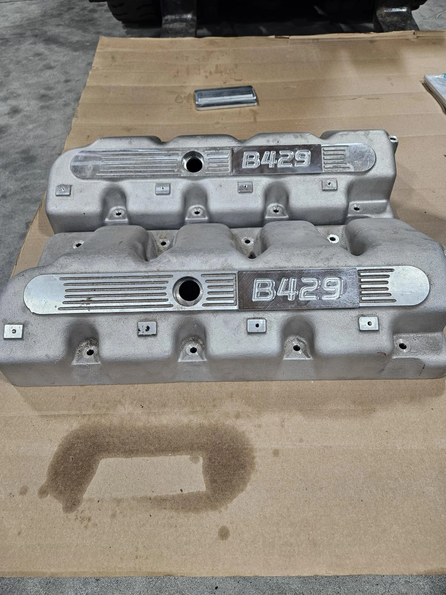 Two metallic engine valve covers labeled 'B429' on a cardboard surface.