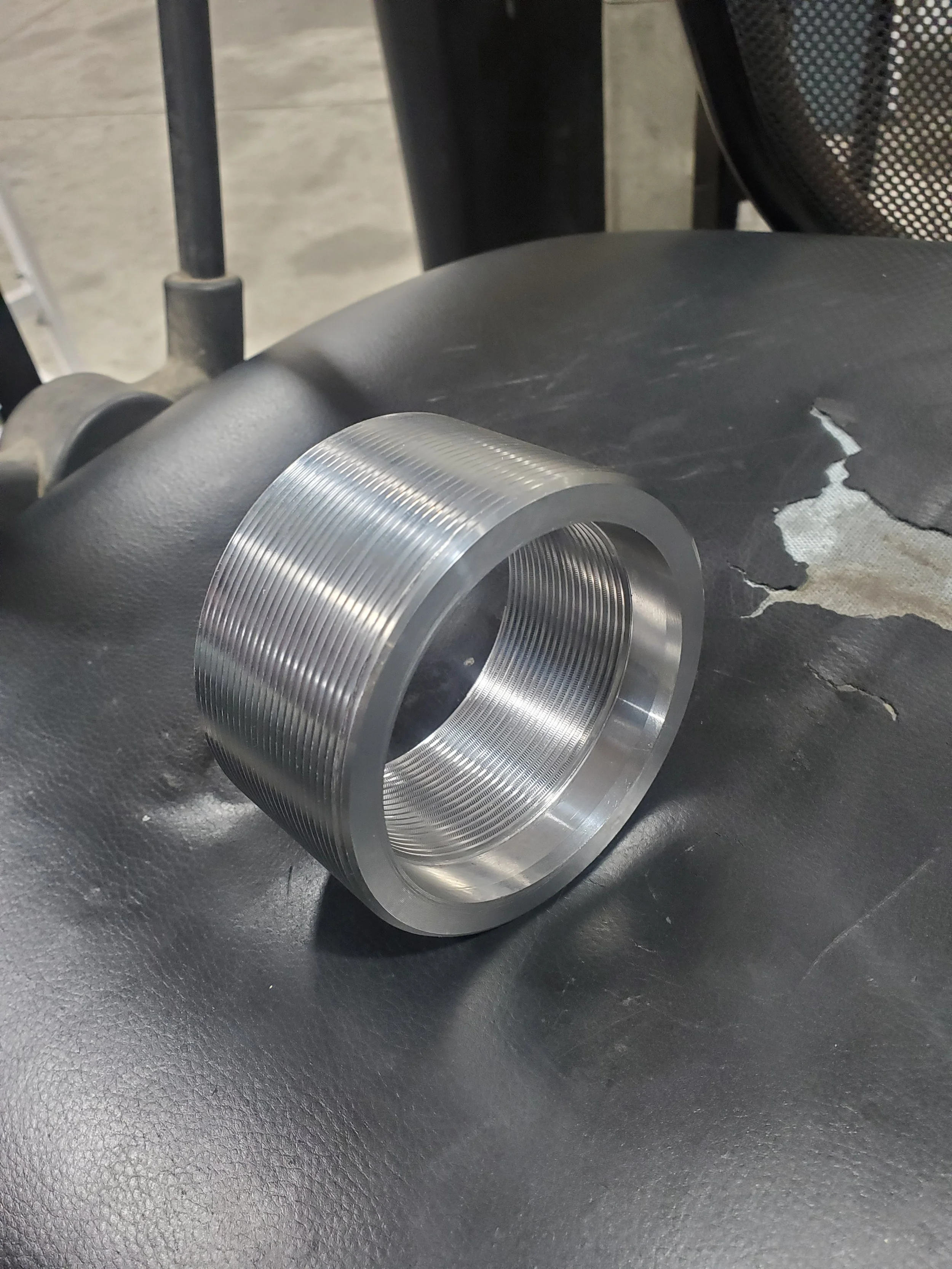 Metal cylinder with threaded exterior, placed on a leather chair.