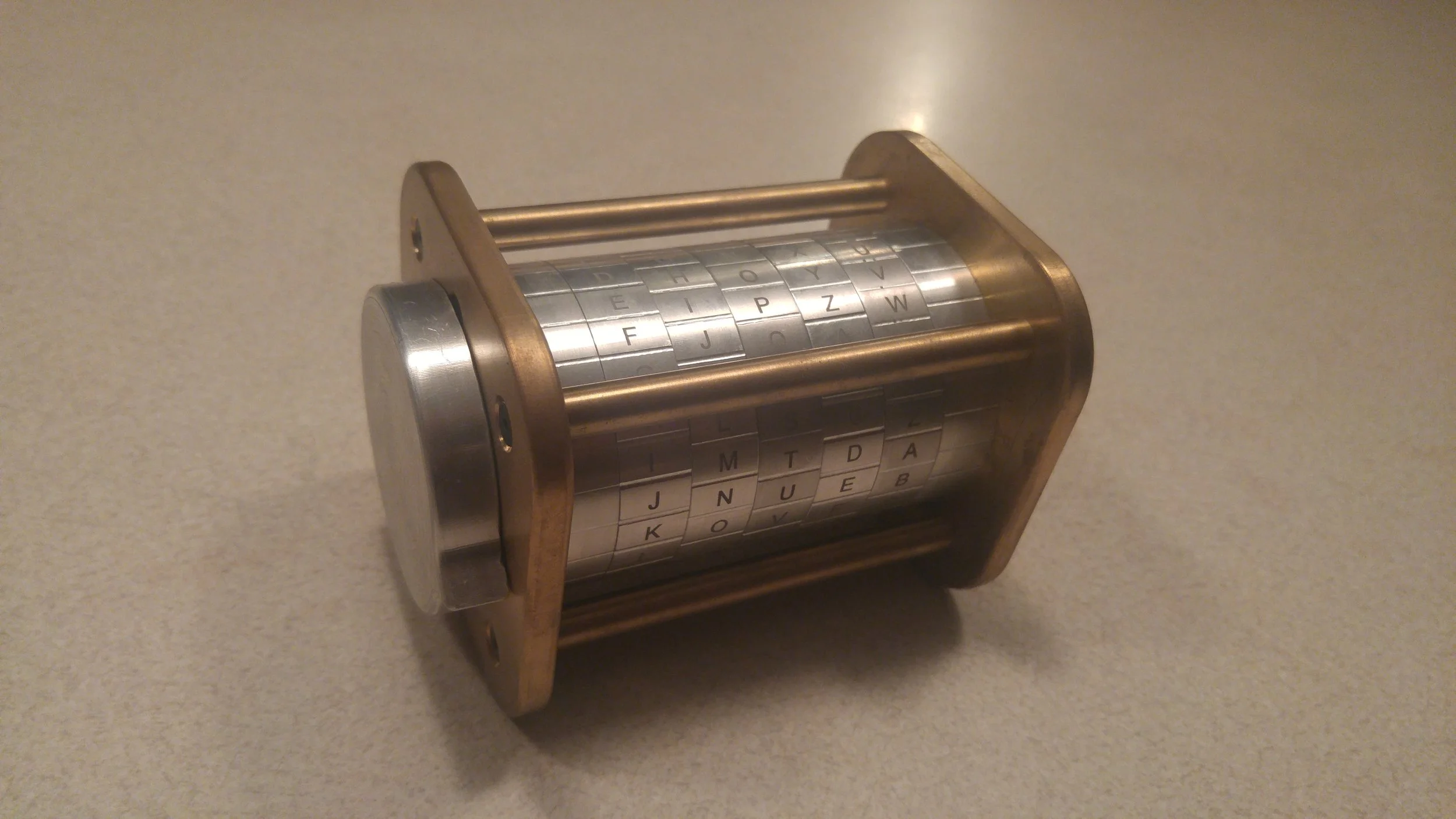 Cryptex puzzle box on a table with metal rings featuring letters in a grid pattern.
