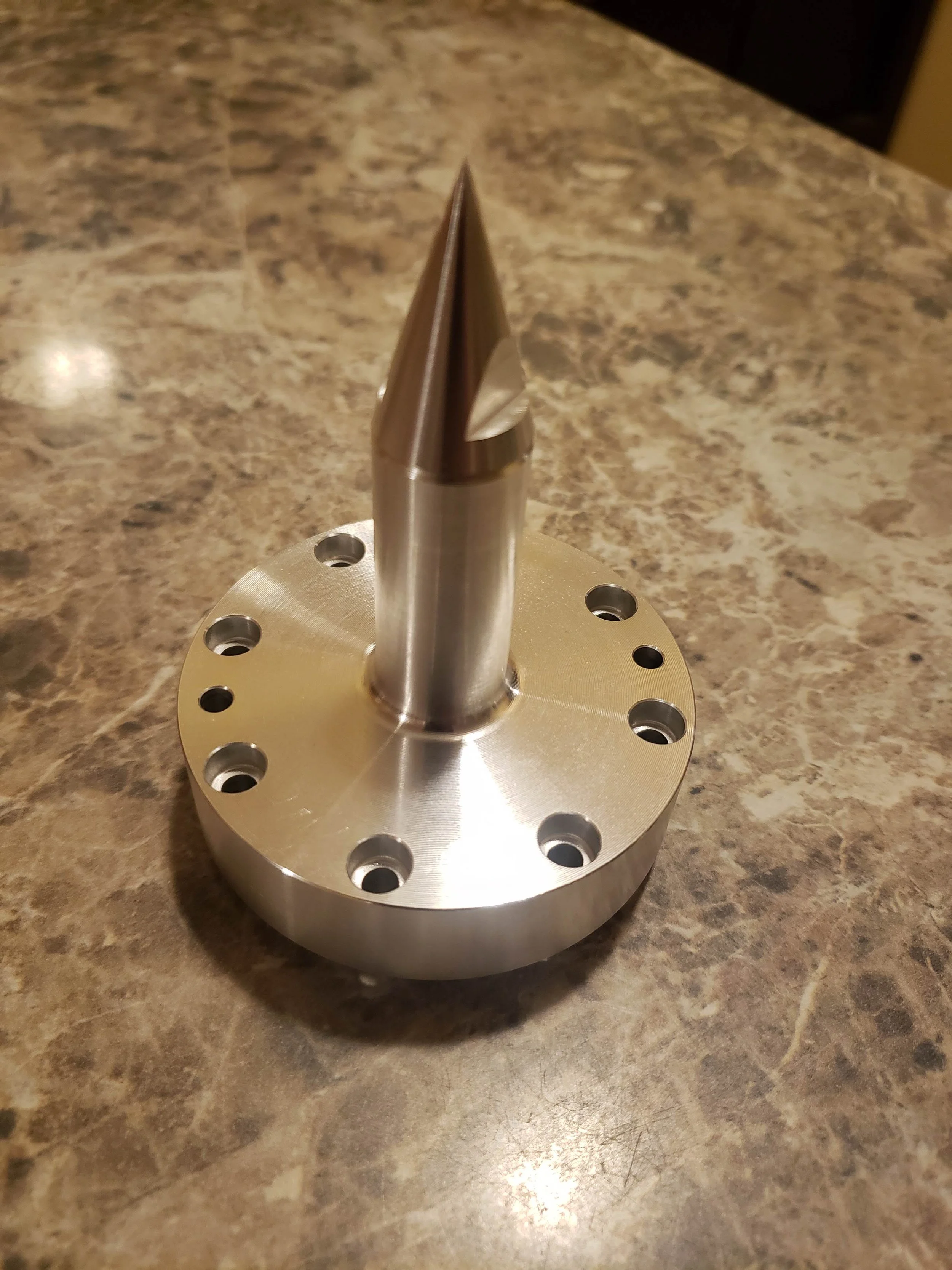 Metal cone-shaped object with a flange and bolt holes on a marble surface