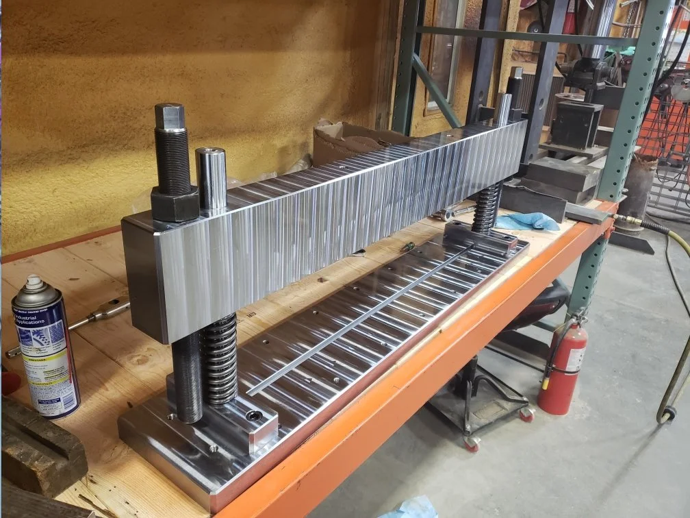 Metal press on a workbench in a workshop with tools and fire extinguisher nearby.