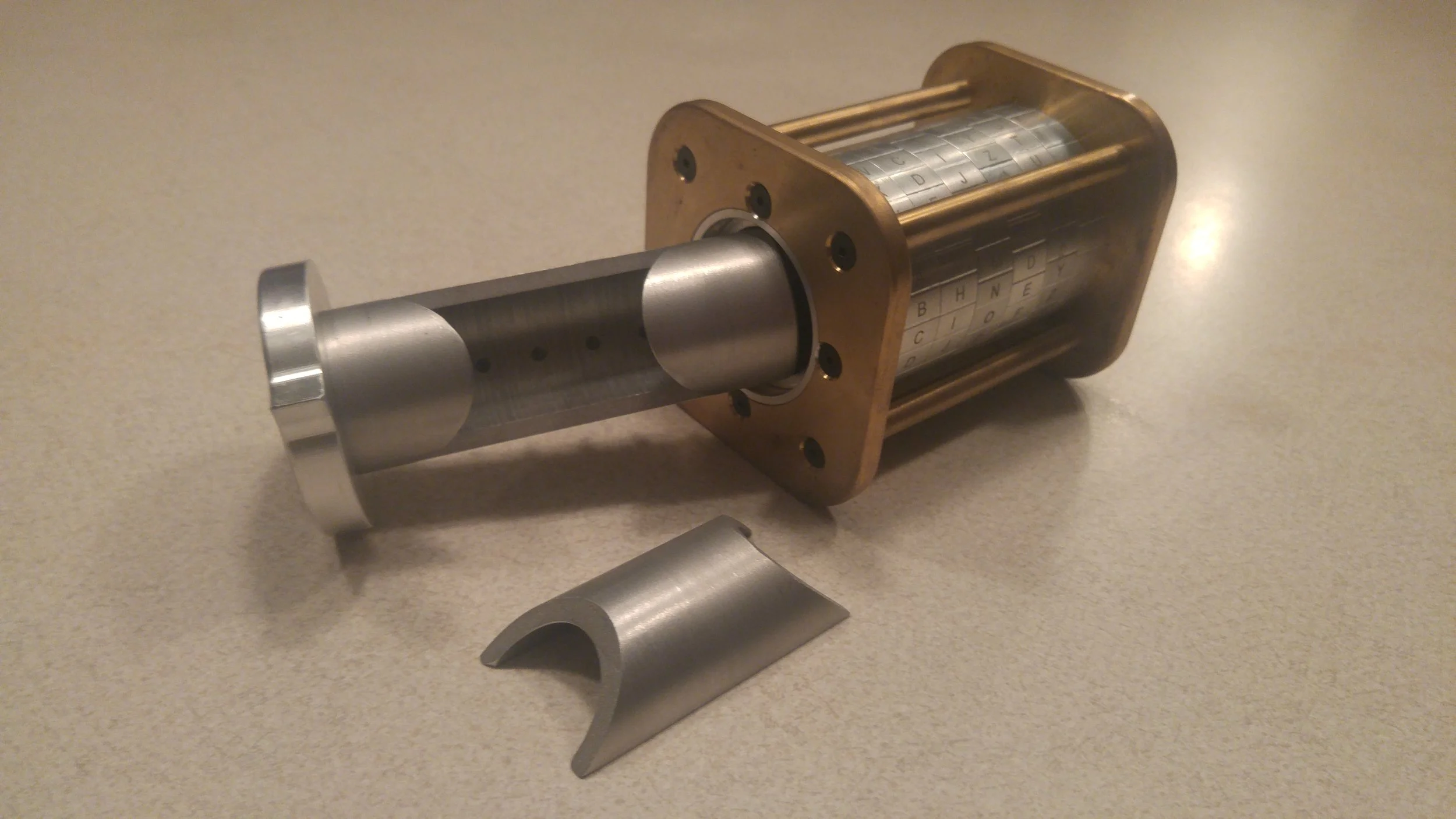 Cryptex with exposed internal components, including metal casing and lettered dials, on a beige surface.