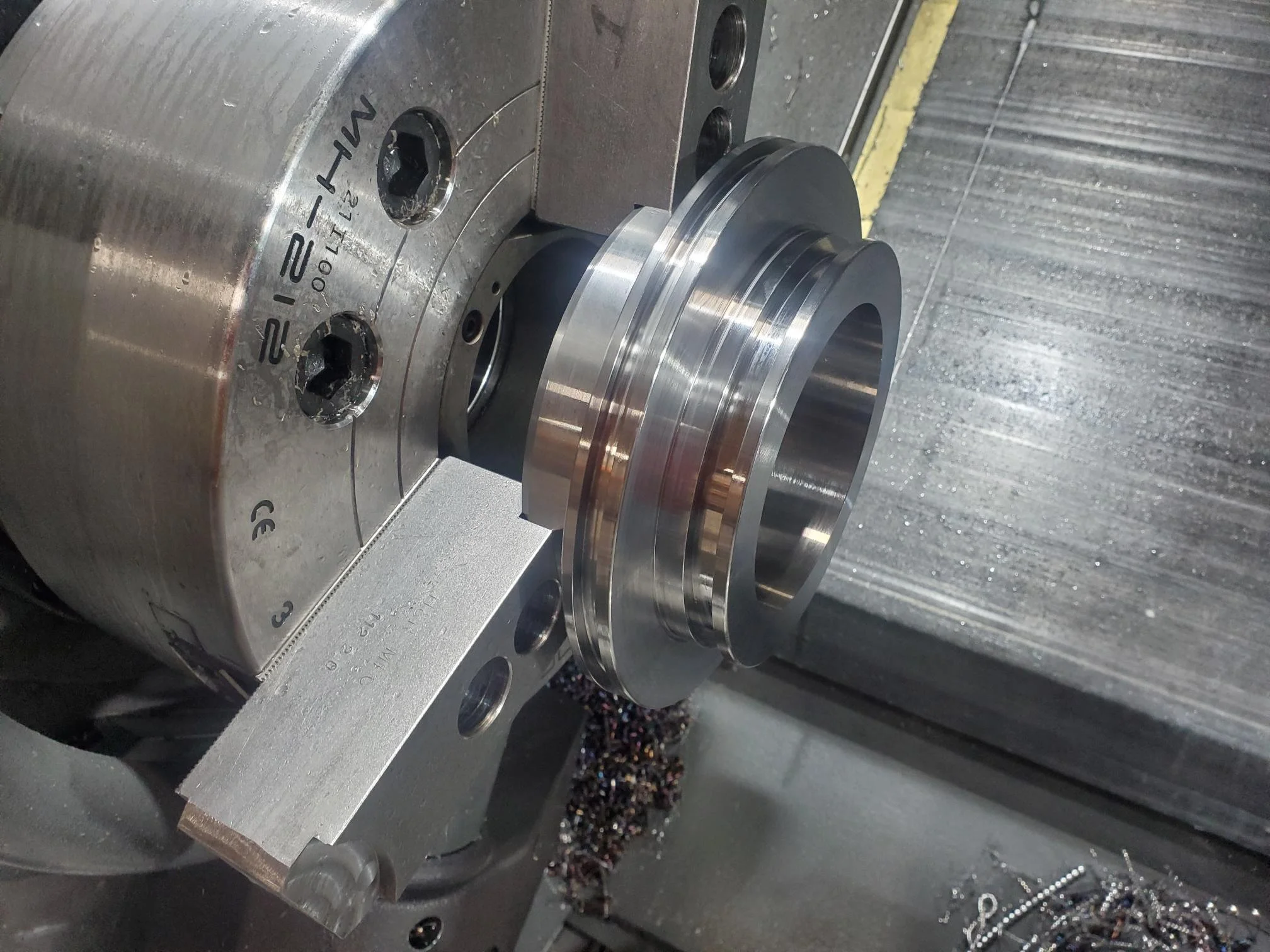 A metal part being machined in a CNC lathe, with visible cutting tool and metal shavings.