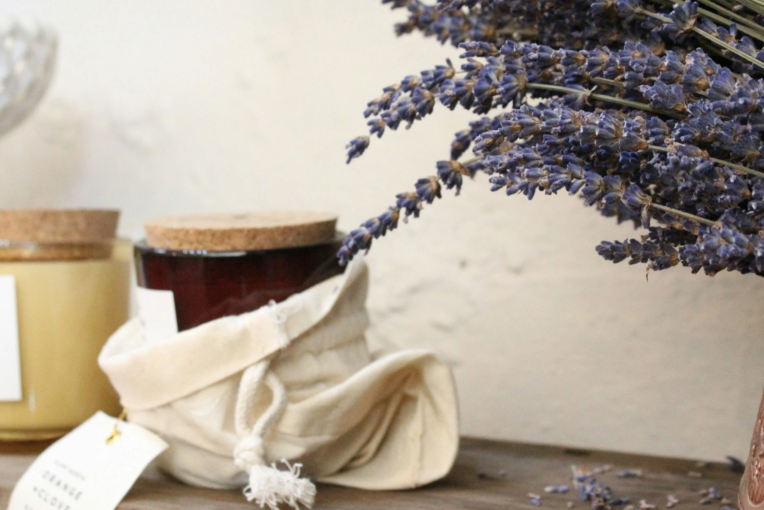 A bouquet of lavender flowers resting on a table alongside jars of cream or honey with cork lids.