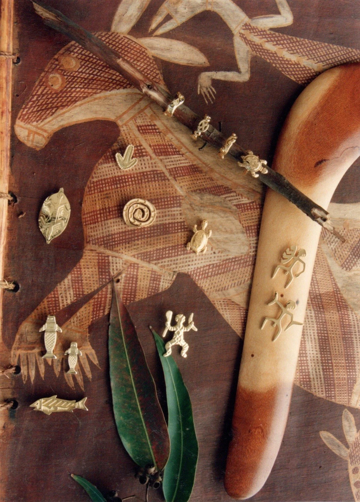 Assorted jewelry charms and decorative objects laid out on a wooden surface with leaves and tribal patterns.