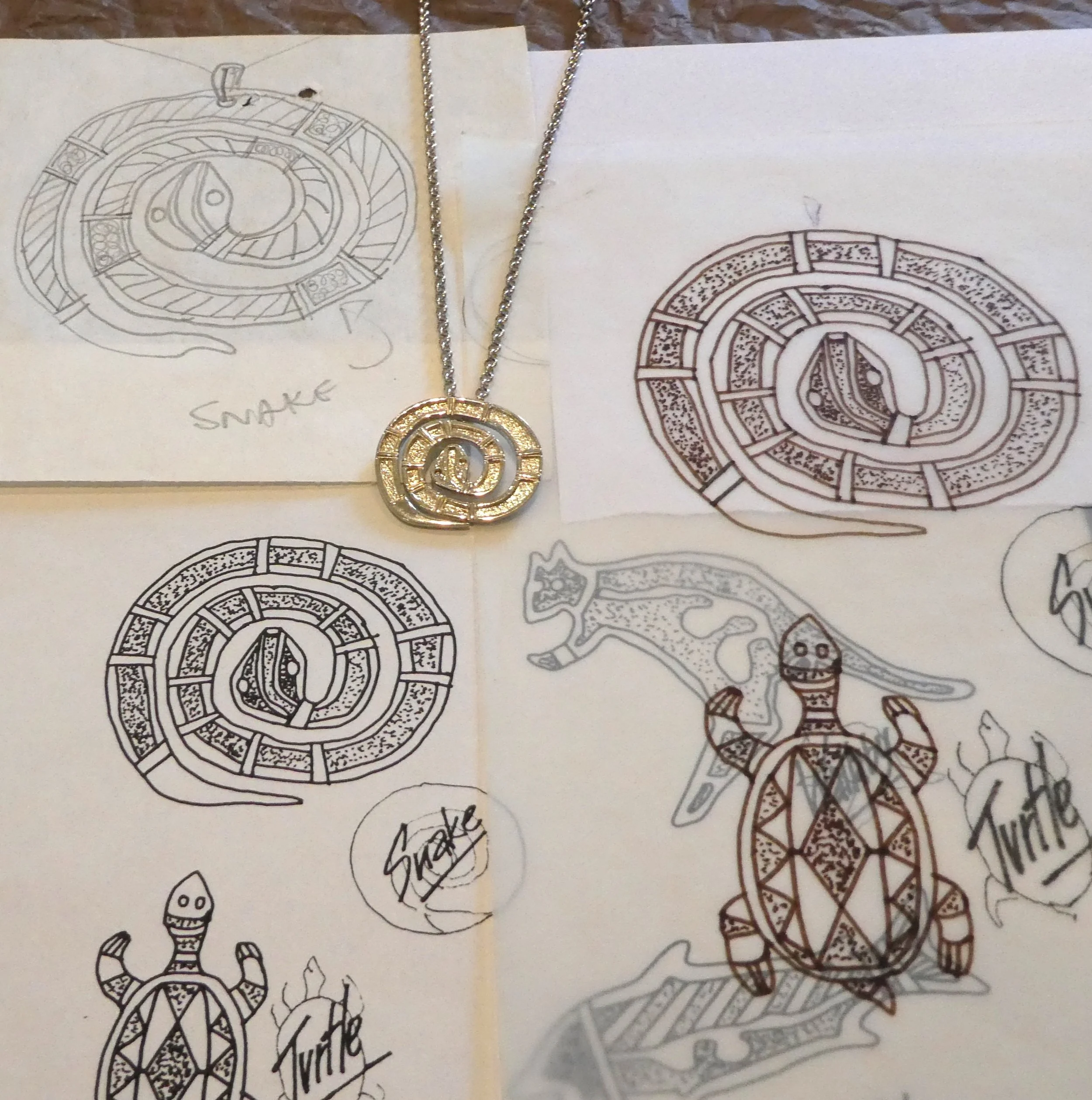 Drawings of a snake, turtle, and a turtle with a snake's head, along with a necklace featuring a circular pendant with a maze design.