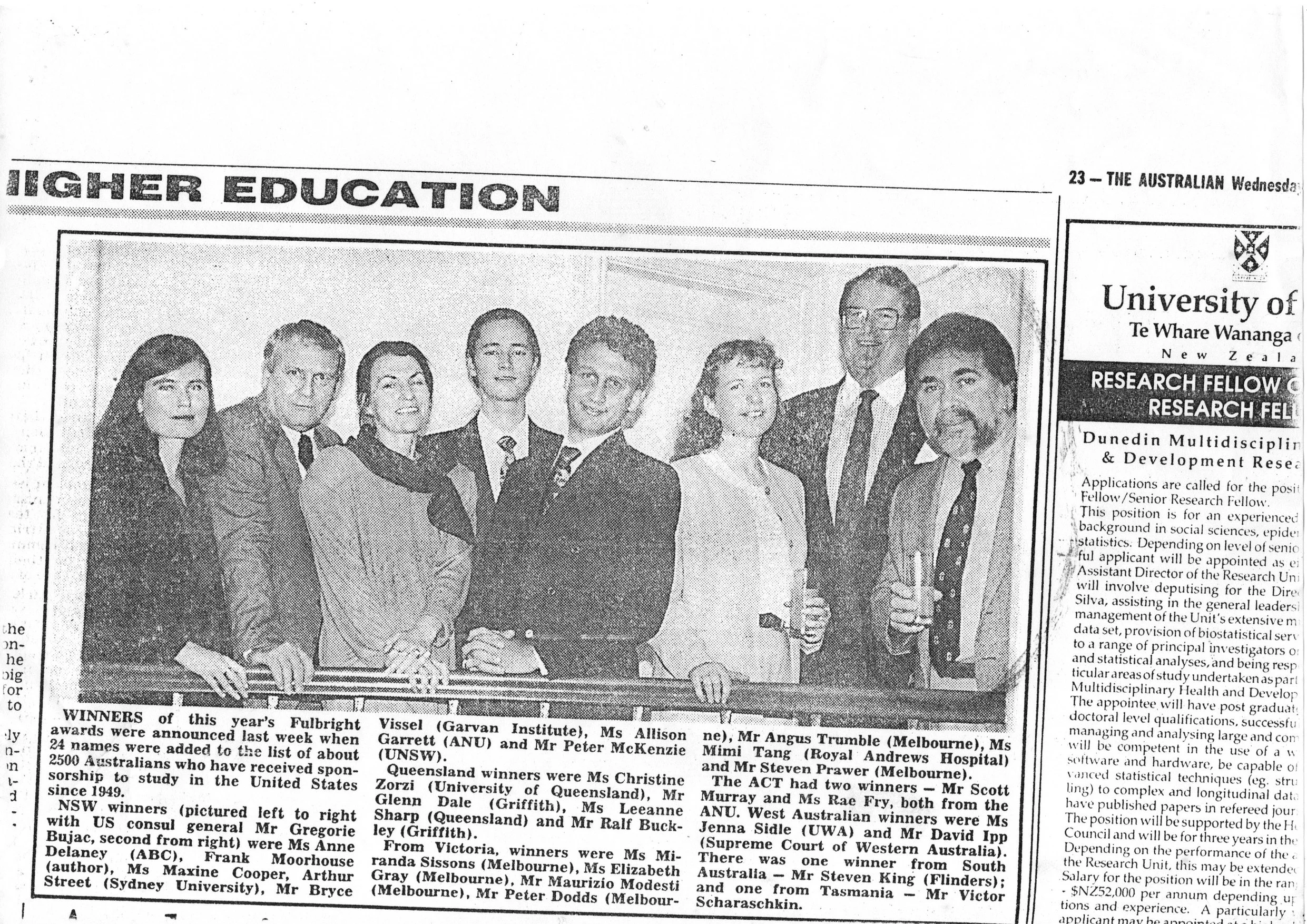 Black and white photograph of a group of nine people standing together indoors, dressed in formal attire, smiling at the camera.