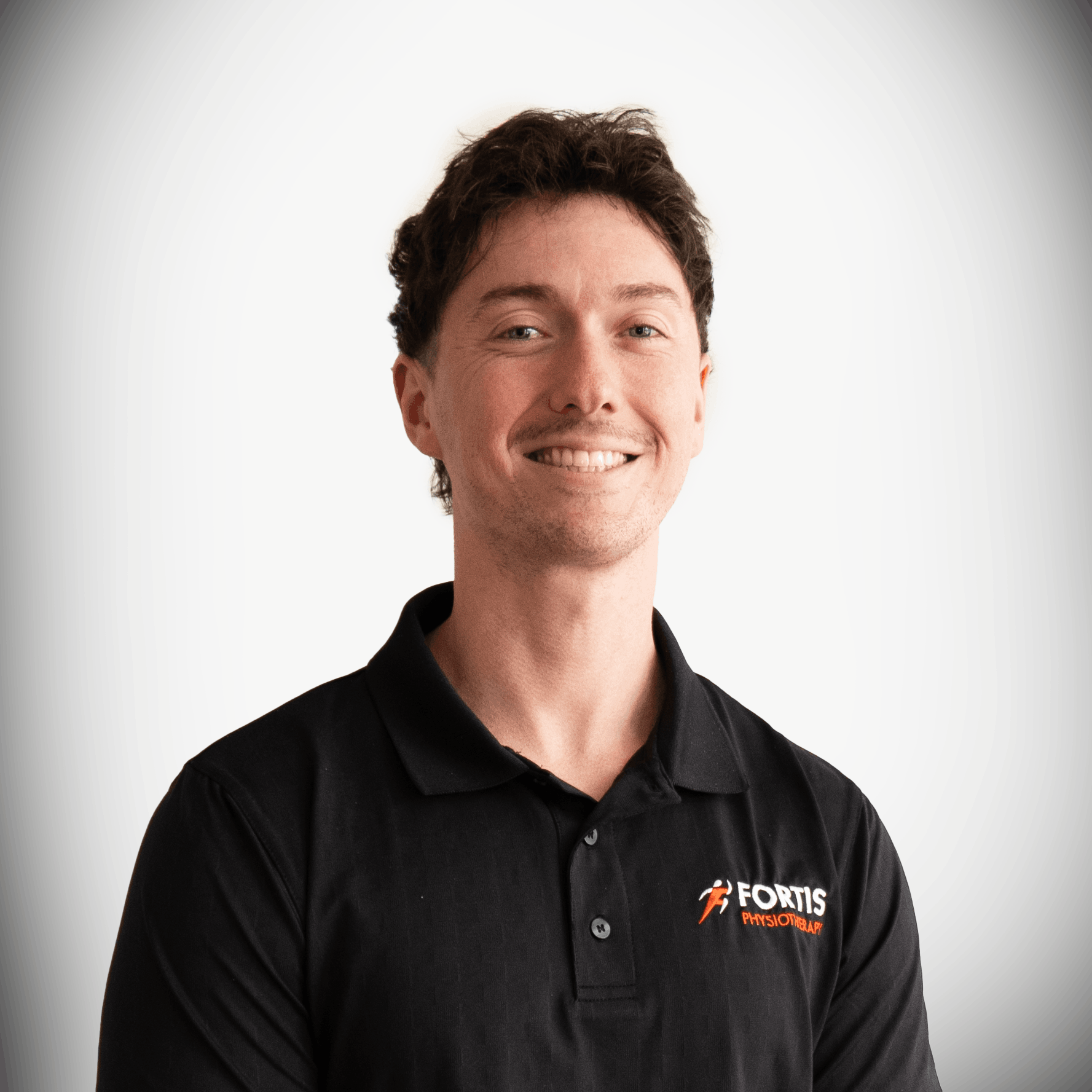 A young man with short brown hair and fair skin, wearing a black collared shirt with a logo that reads "Fortis Physiotherapy and Rehab," smiling in front of a white background.