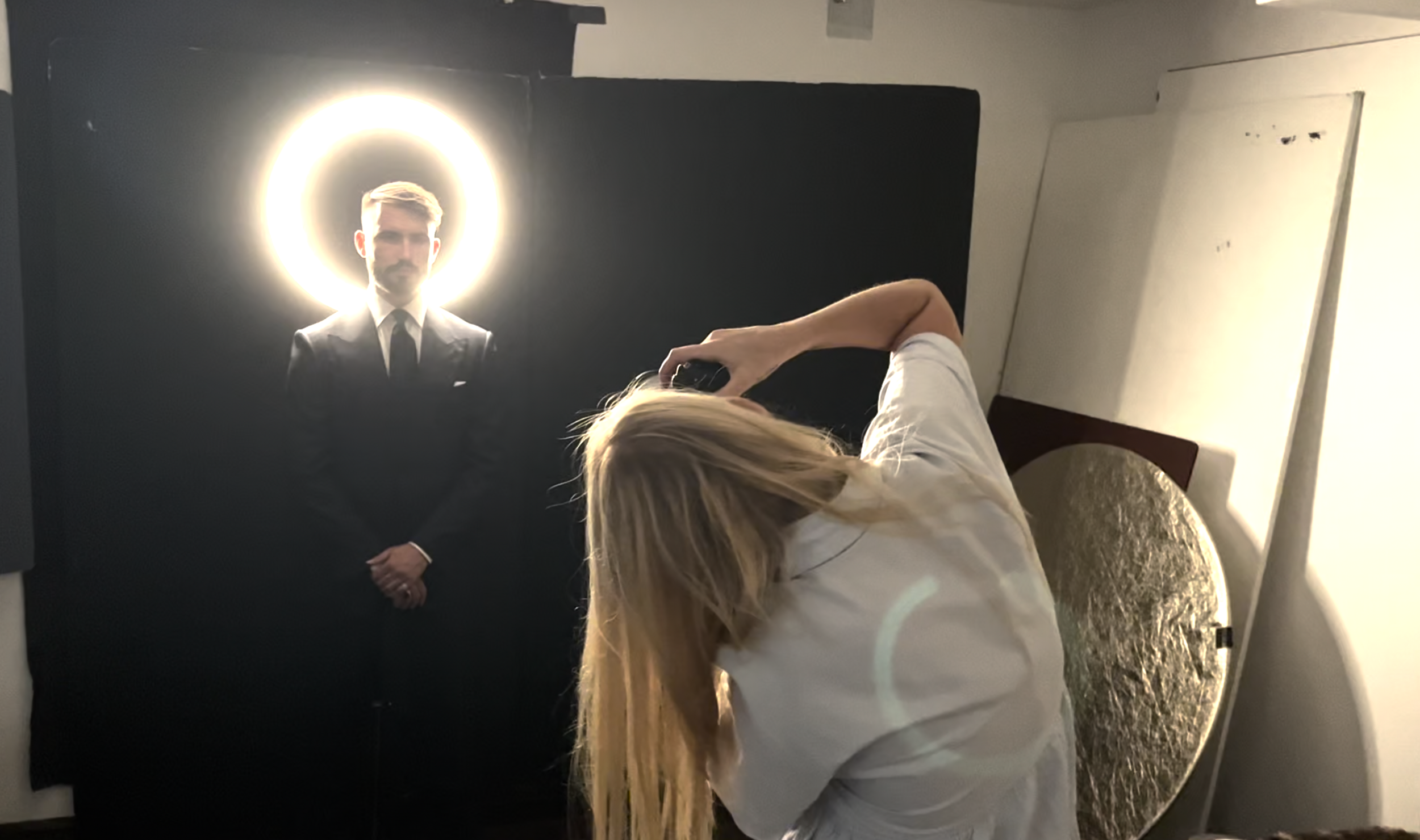 Photographer taking a portrait of a man in a suit with a halo-like light behind his head in a studio setting.
