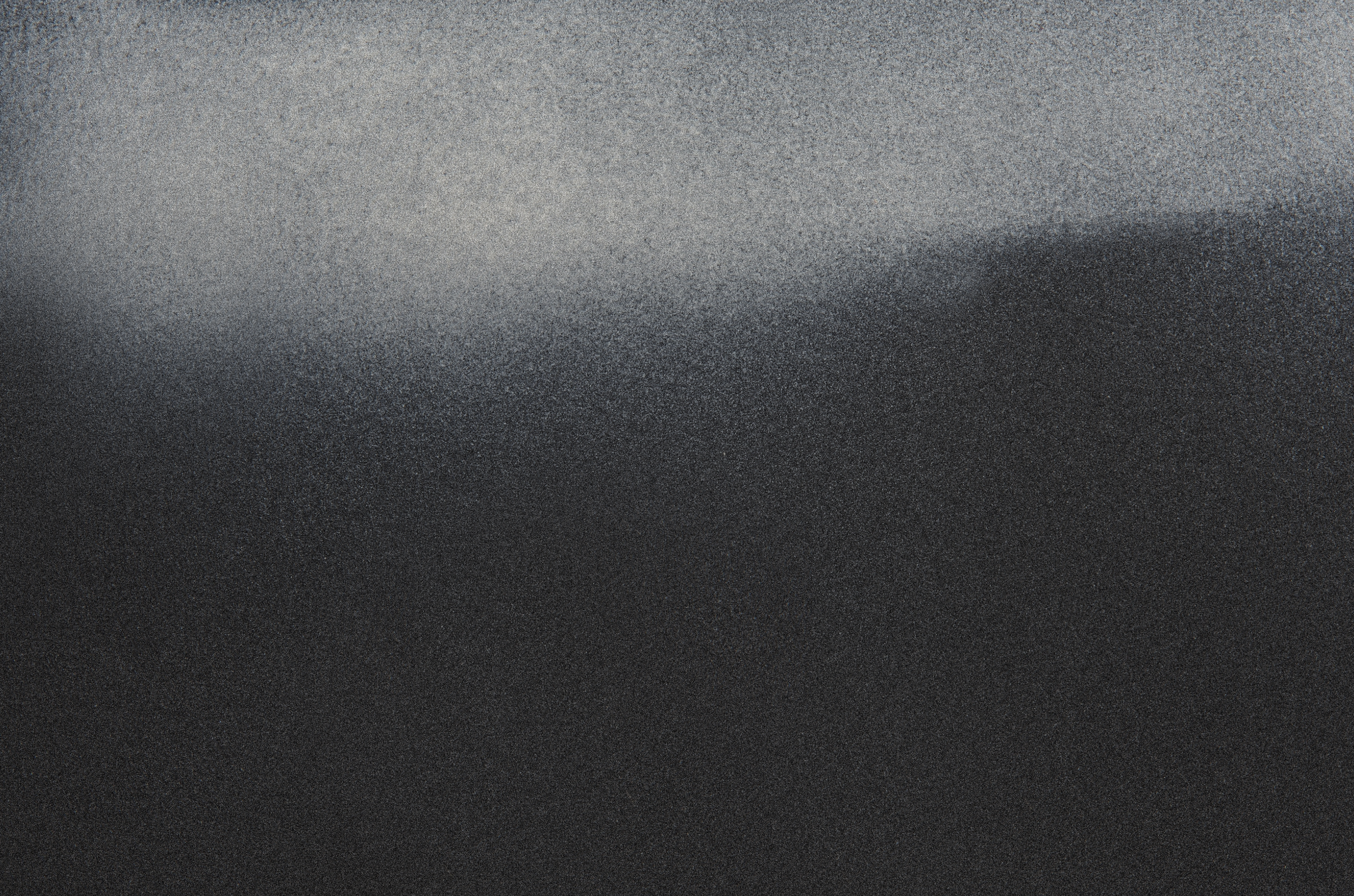 A monochrome gradient of gray tones, darker at the bottom and lighter at the top, with a textured surface that appears grainy or speckled.