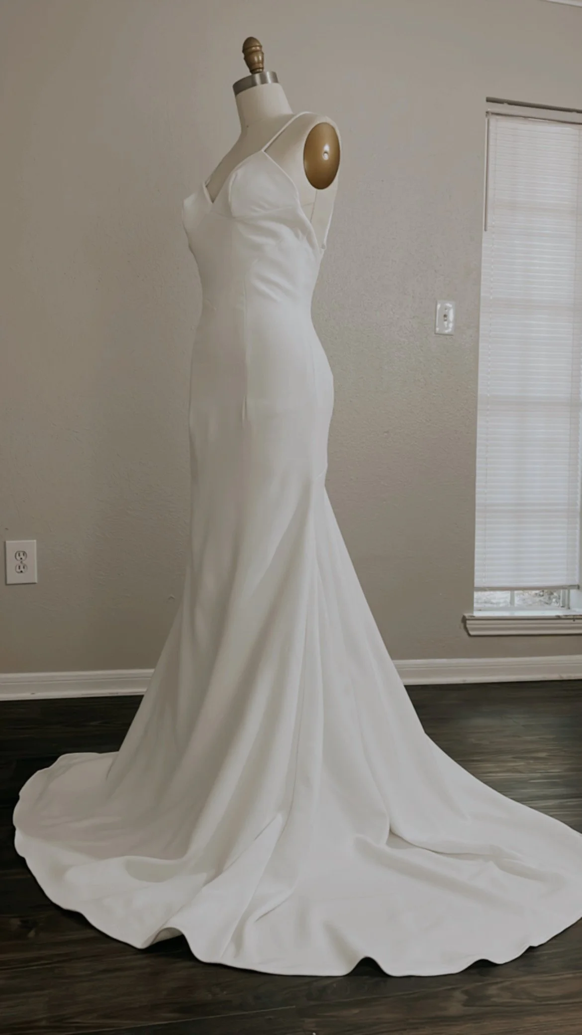 A white wedding dress on a mannequin indoors next to a window