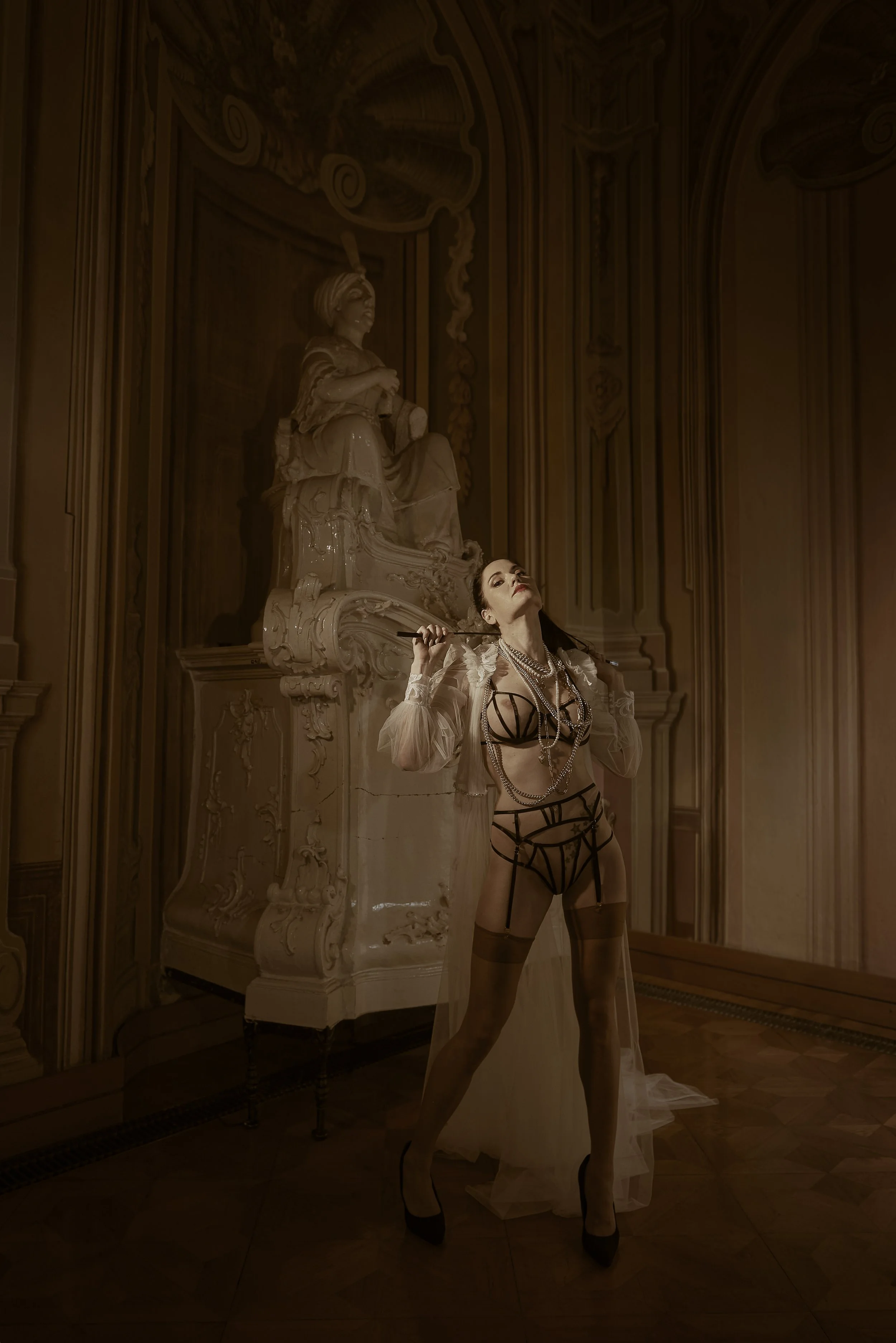 Luxury boudoir photography of a woman in black lingerie with hands up, holding a whip, captured by Amanda Gril, Ljubljana-based boudoir photographer specializing in elegant, cinematic portraits.