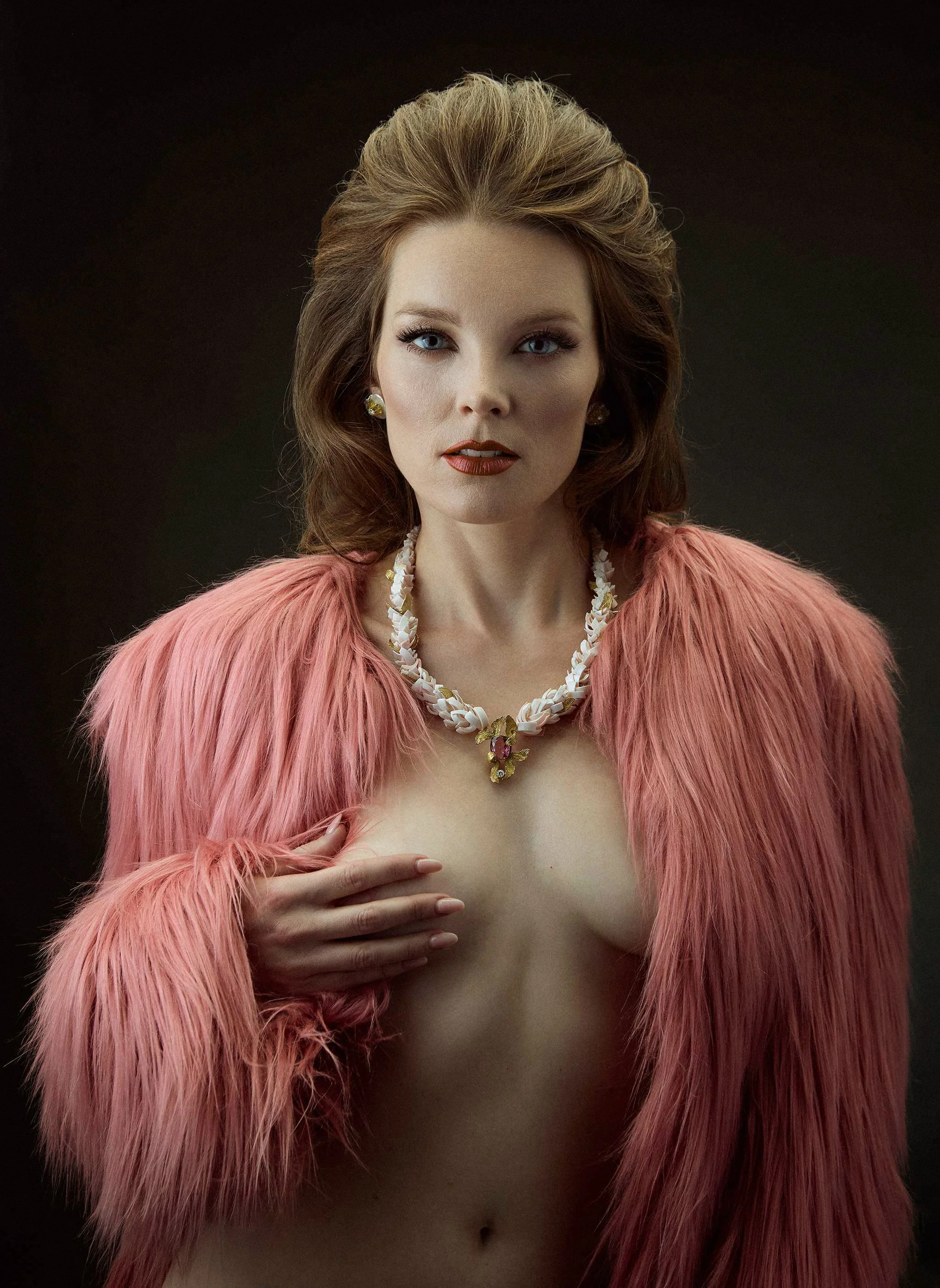 Boudoir portrait of a woman with red hair wearing a pink jacket and stylish necklace, captured in warm vintage-style lighting