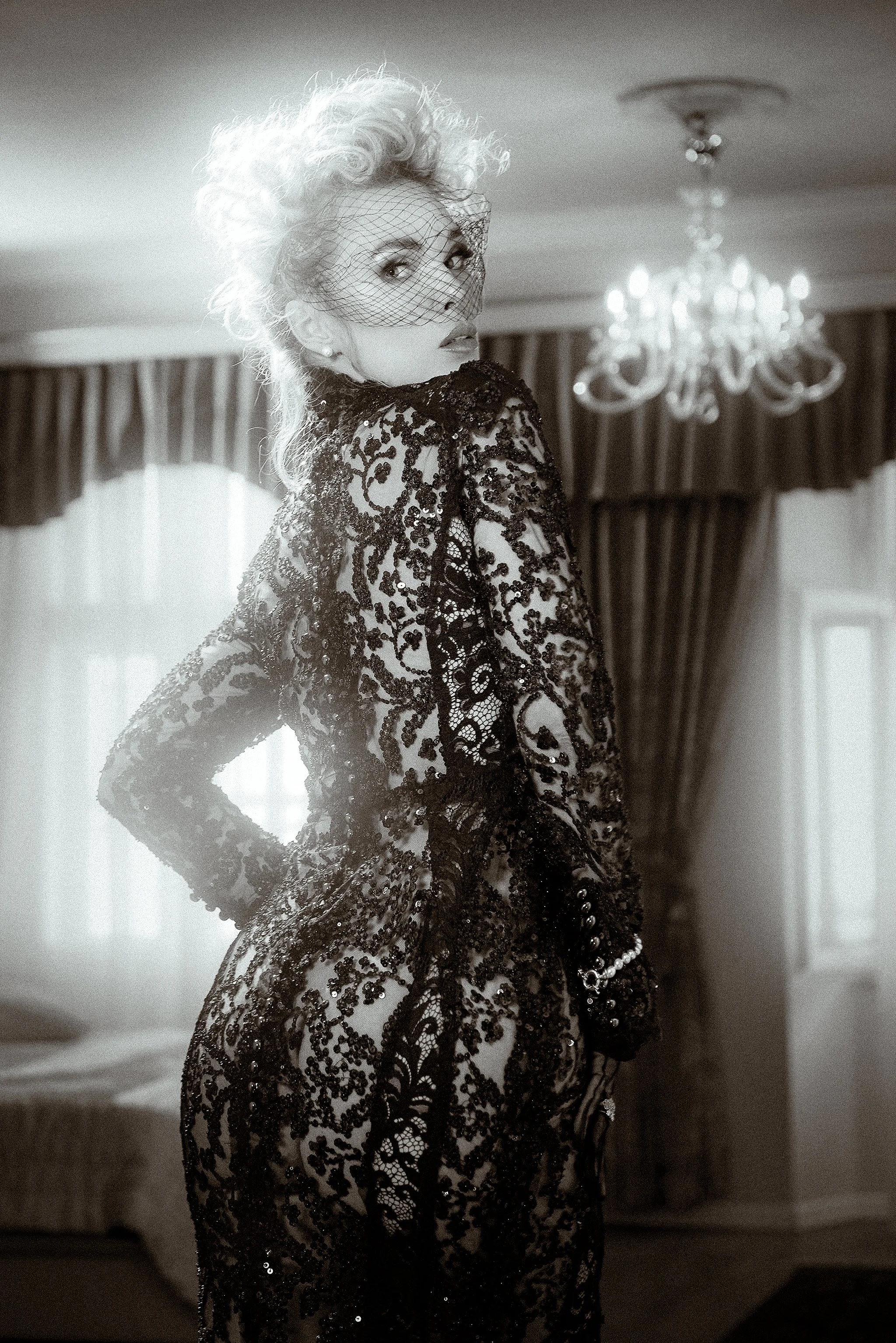 Explore a dramatic black-and-white editorial fashion portrait featuring intricate black lace, vintage glamour styling, and cinematic interior light.